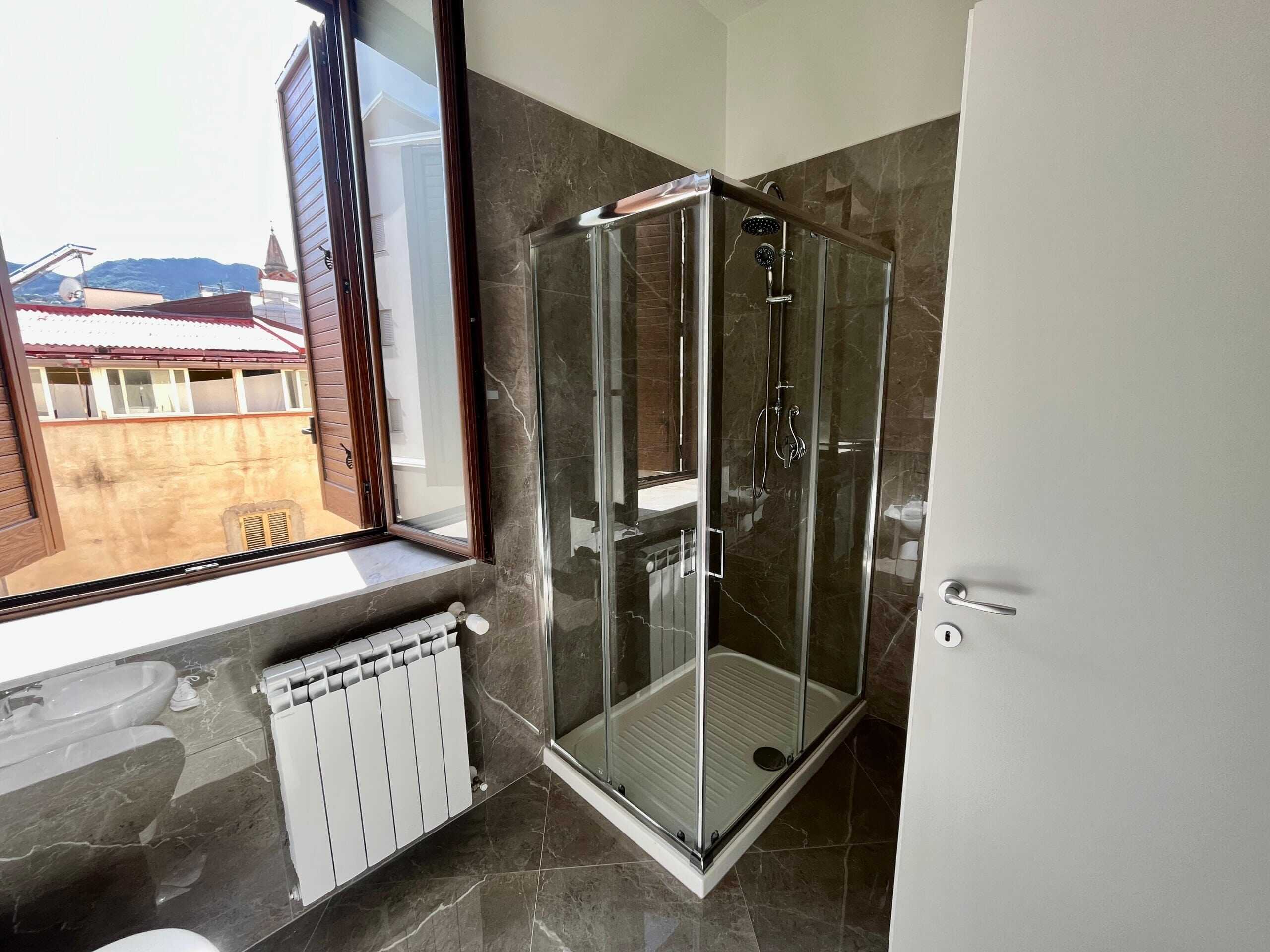 Vasca-doccia-in-vetro-trasparente-con-muratura-in-marmo-marrone-interno-di-una-casa-con-finestra.