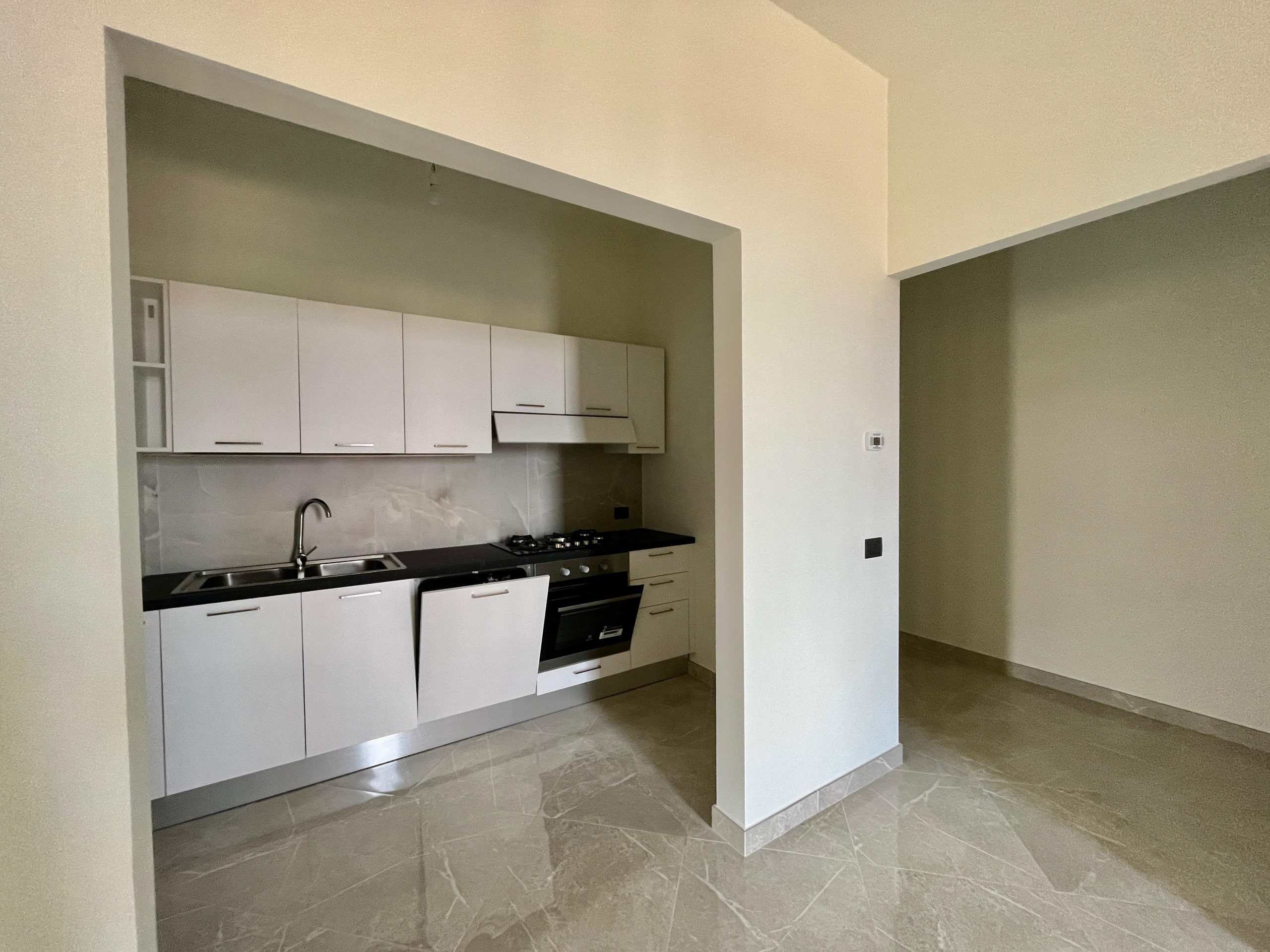 Cucina moderna con mobili bianchi, piano in nero, area open space, pavimento in gres effetto marmo, casa nuova, interior design minimalista, NextCasa.
