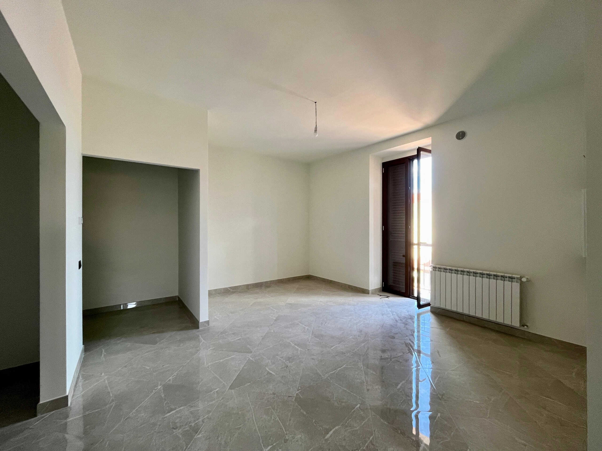 Ampio soggiorno con balcone, finestra e radiator, spazio luminoso e moderno, ideale per vivere e arredare con stile.