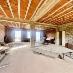 Ristrutturazione edificio residenziale con interni in fase di completamento, pareti in mattone e soffitto con travi di legno, ambiente ampio e luminoso.