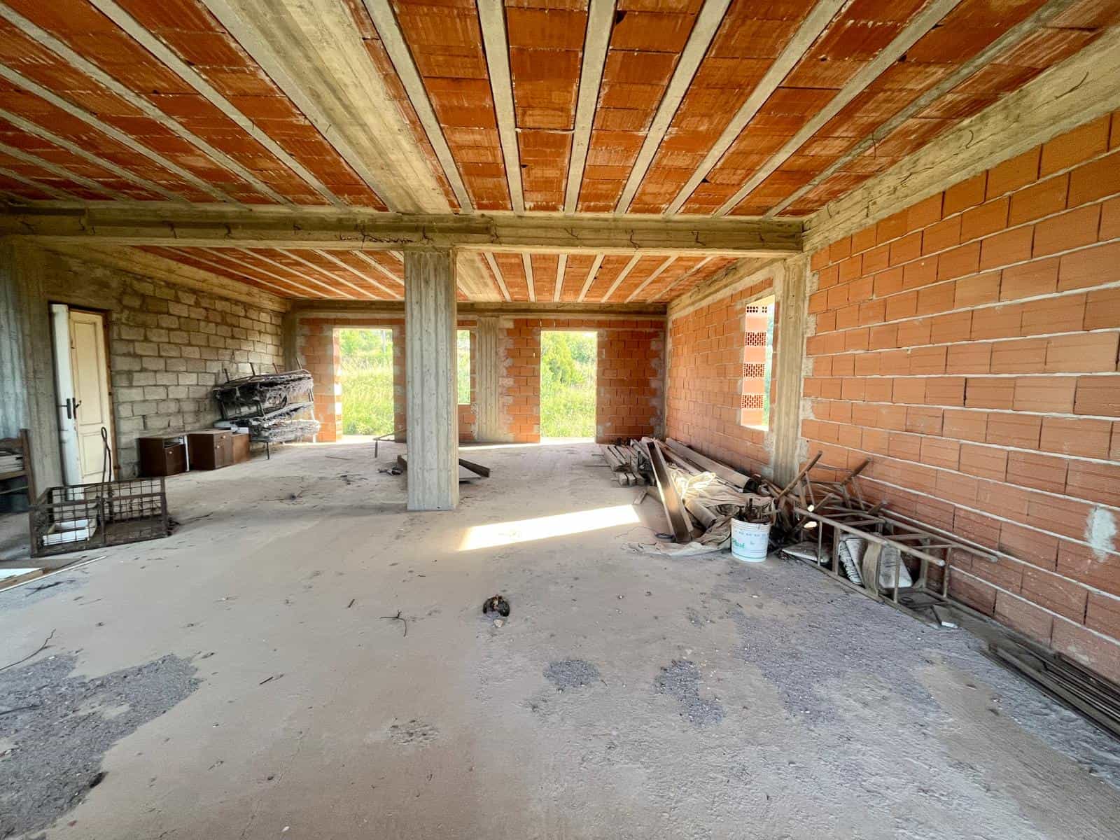 Ampio spazi interni di una casa in costruzione con pareti in mattoni, soffitto in legno e cemento. Ambiente aperto con luce naturale e materiali di costruzione visibili, ideale per progetti di ristrutturazione e nuove abitazioni.