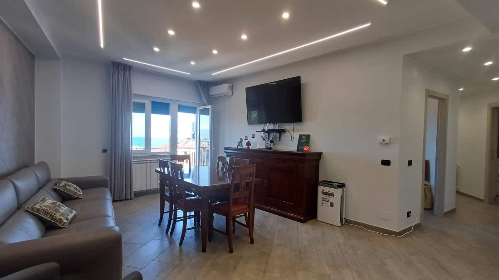 Spazioso soggiorno con vista mare, divano in pelle, tavolo da pranzo in legno, televisore a schermo piatto e aria condizionata, ideale per case vacanza di charme.