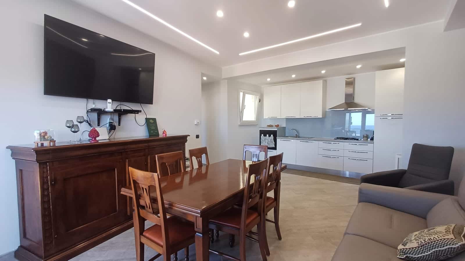 Ampio soggiorno e cucina moderna con arredi eleganti, TV a schermo piatto, dettagli di design, pareti bianche, illuminazione a LED, stile minimalista e accogliente, ideale per vivere e socializzare.