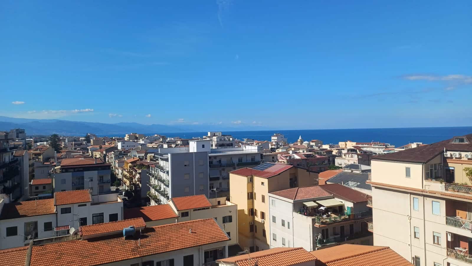 Ville di mare con edifici residenziali e tetti in terracotta, vista panoramica sul mare e sul cielo azzurro, immobile di pregio in località balneare, opportunità immobiliare NextCasa.