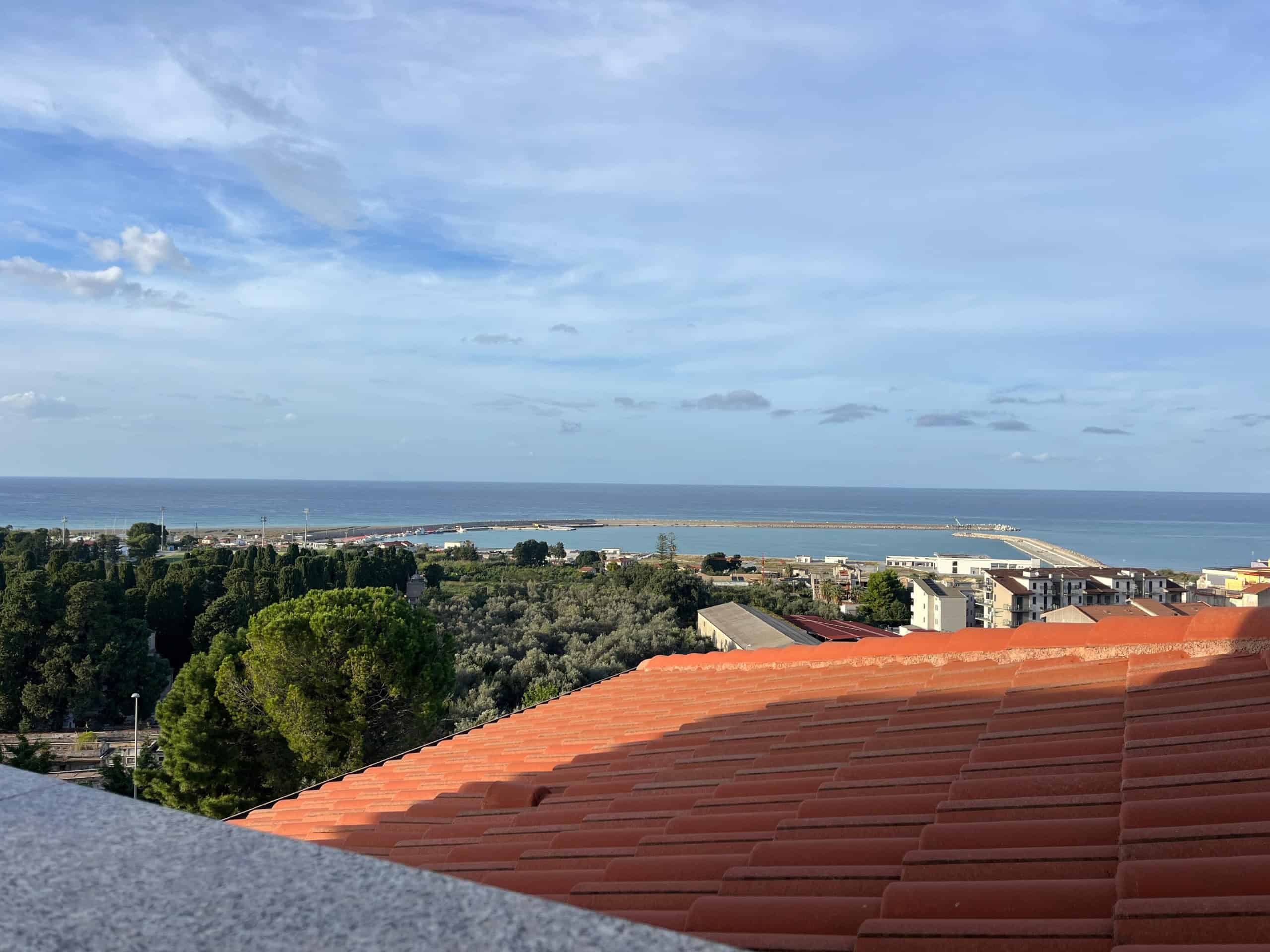 VISTA MARE DALLA TERRAZZA DI UNA CASA IN AFFITTO A VASTO MARINA, IN ABRUZZO, CON TETTO IN PIETRA E VERDE STRADA DAGLI ALBERI ALL'ORIZZONTE.