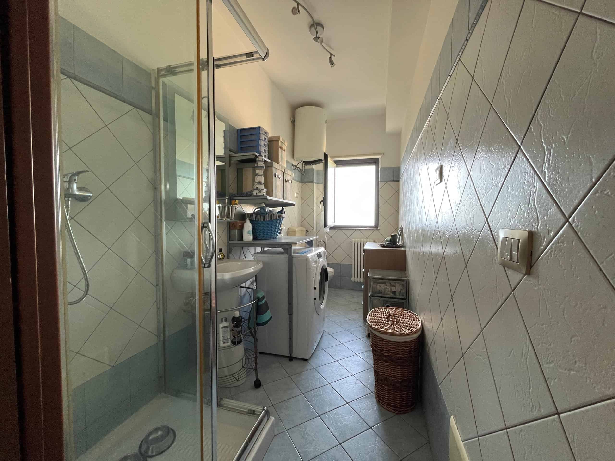 Lavanderia spaziosa con angolo lavatrice, asciugatrice, scaffali e biancheria, dotata di finestra, ideale per organizzare vestiti e pulizie domestiche.