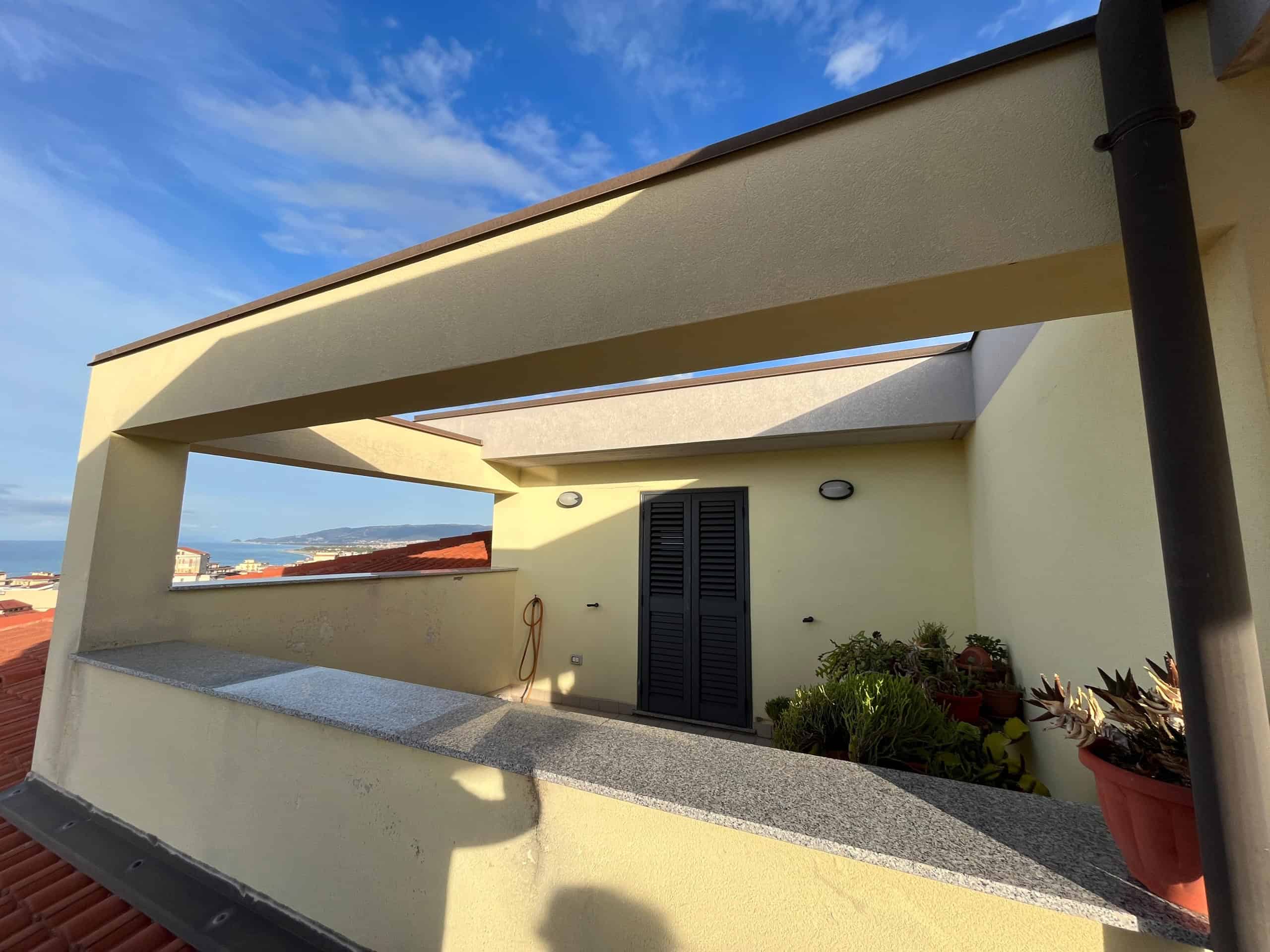 Panorama ampio terrazzo con vista mare, superficie rifinita con pietra e piante in vaso, ideale per relax e arredamento esterno, immerso nella luce naturale e con un tetto parapetto in cemento.