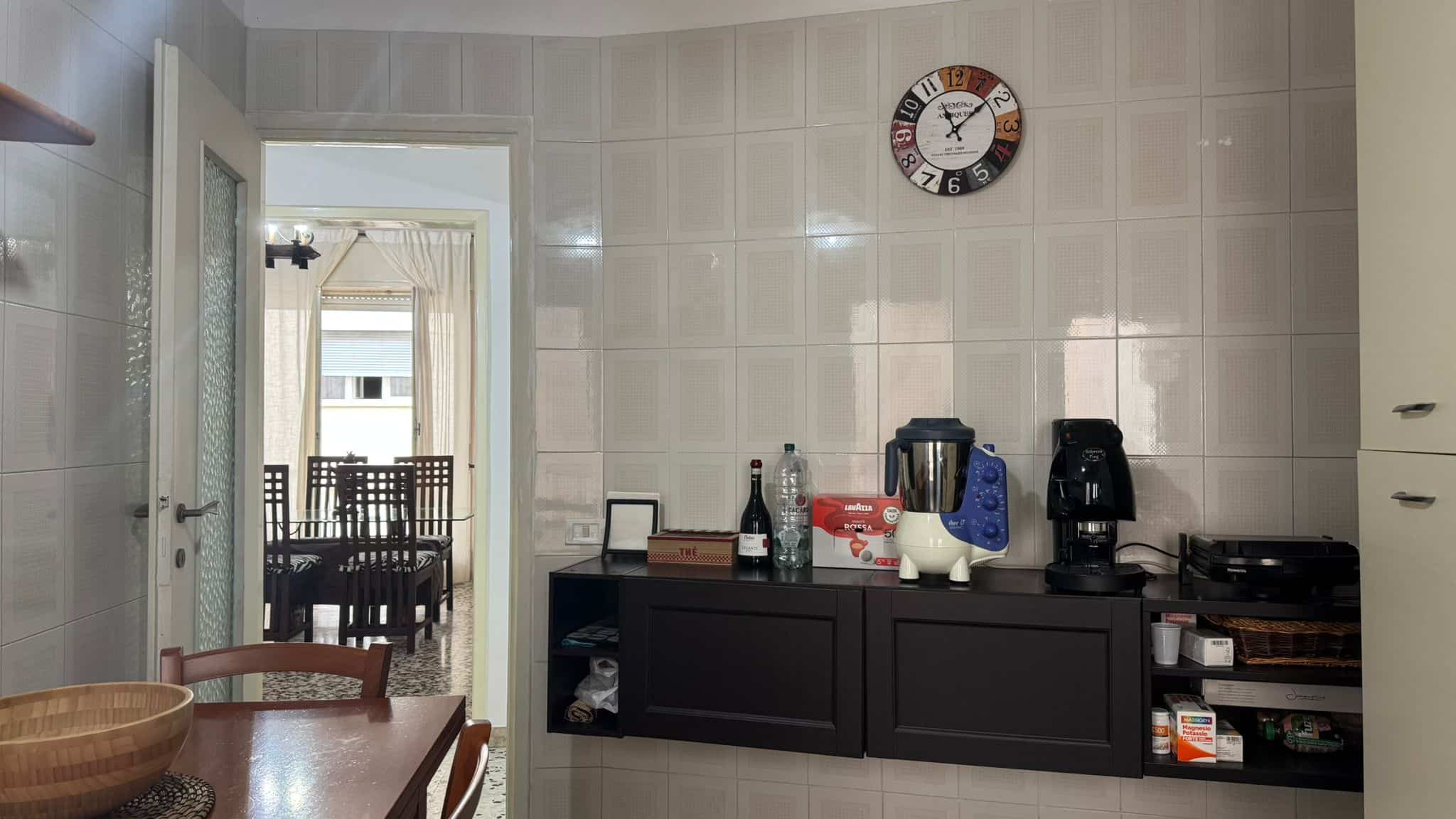 Lavagna a muro con orologio in cucina, pannelli di rivestimento effetto decorativo, elettrodomestici da cucina e oggetti di uso quotidiano, spazio funzionale e moderno.