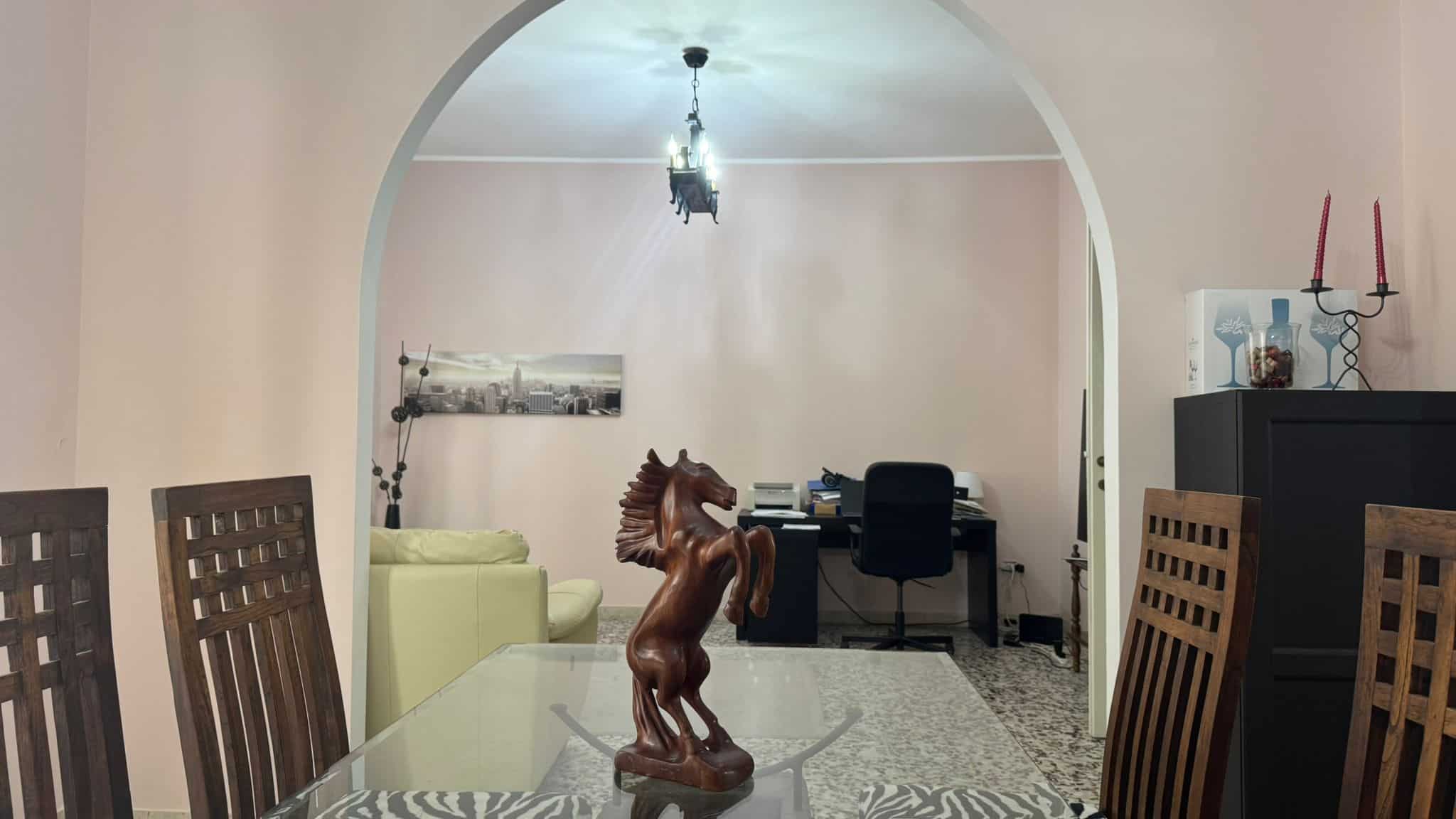 Scultura in legno di un cavallo al centro di una sala da pranzo con tavolo in vetro e sedie in legno, arredo moderno e atmosfera accogliente.