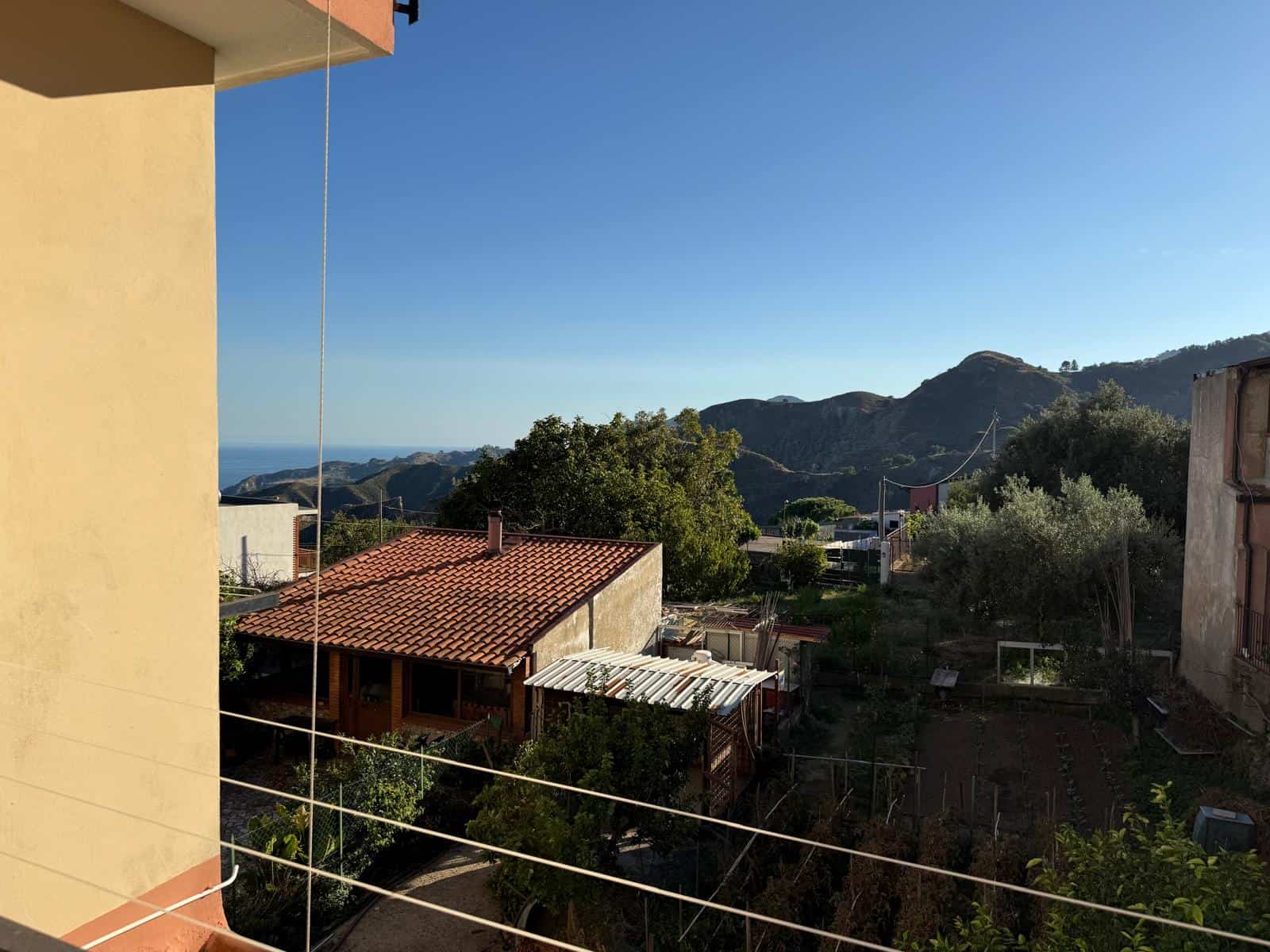 Panorama di un'area residenziale con case circondate da montagne, vista dal balcone di un appartamento, con cielo limpido e natura verde, ideale per immobili e case in vendita o affitto.