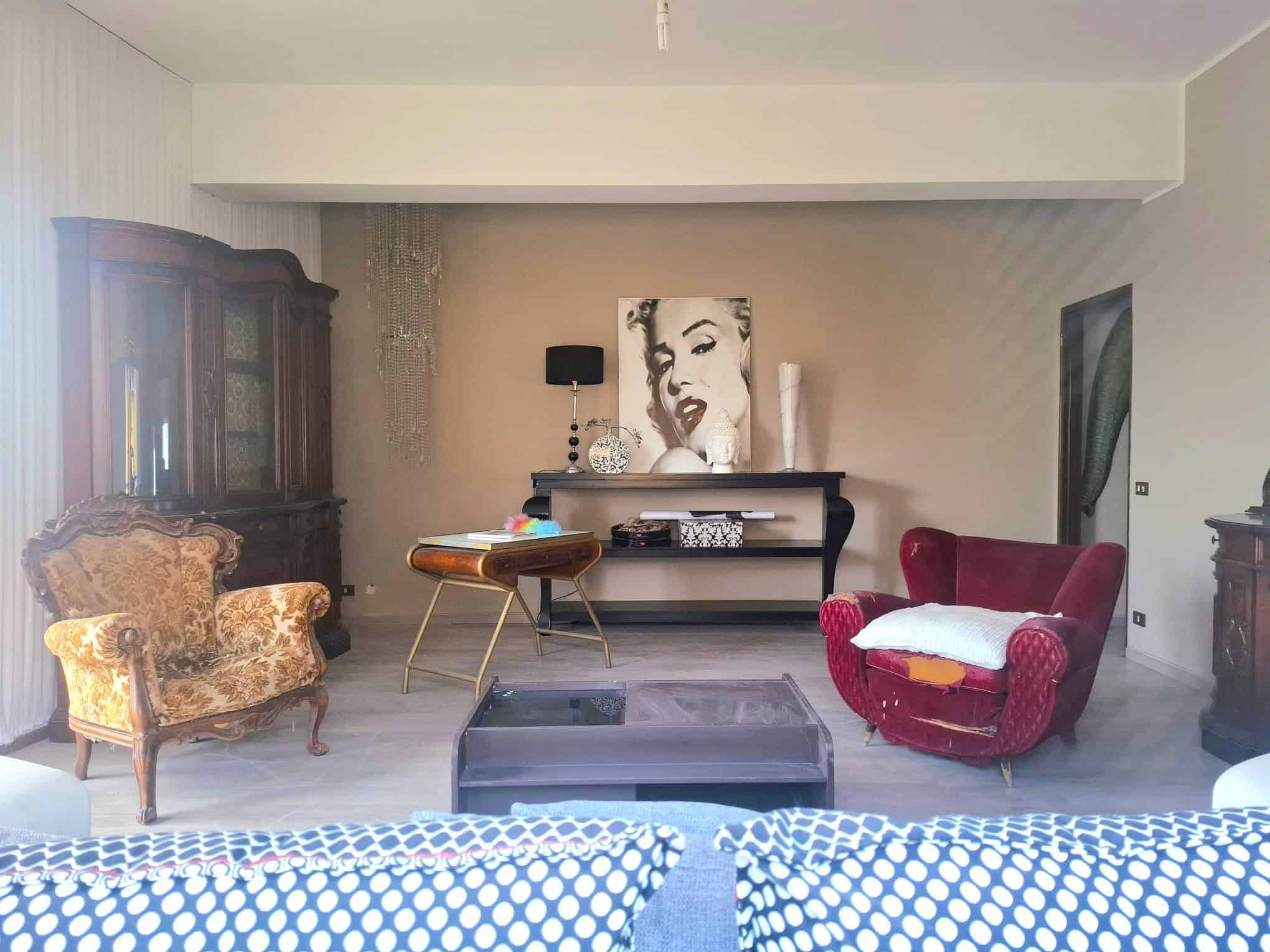 Elegante soggiorno con arredi classici e moderni. Ampio soggiorno con arredi classici e moderni, decorato con un quadro artistico e lampade eleganti, ideale per vivere momenti di relax e convivialità.