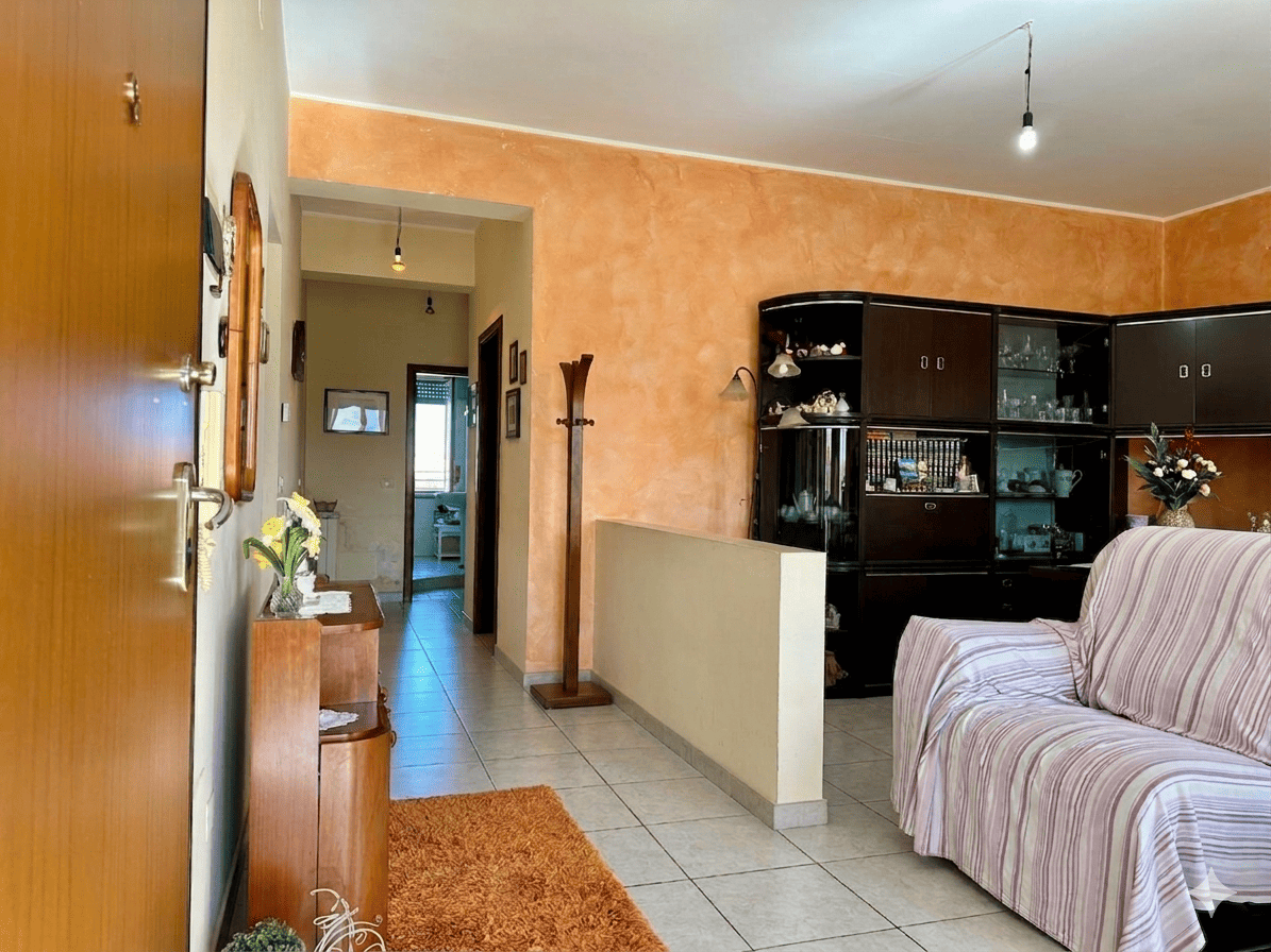 Ampia vista del soggiorno con pareti color pesca, arredi classici e un grande mobile in legno scuro con vetrine, ideale per l'esposizione di oggetti decorativi e stoviglie.