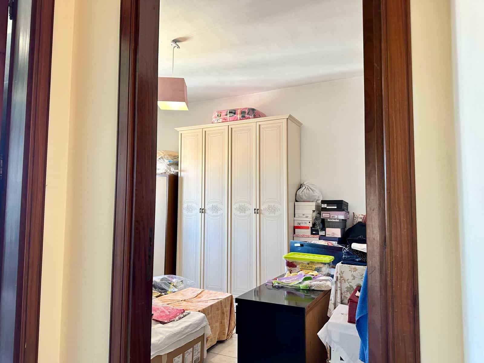 Armadio bianco con design classico in una stanza disordinata con scatole e oggetti vari, vista attraverso una porta in legno massiccio.
