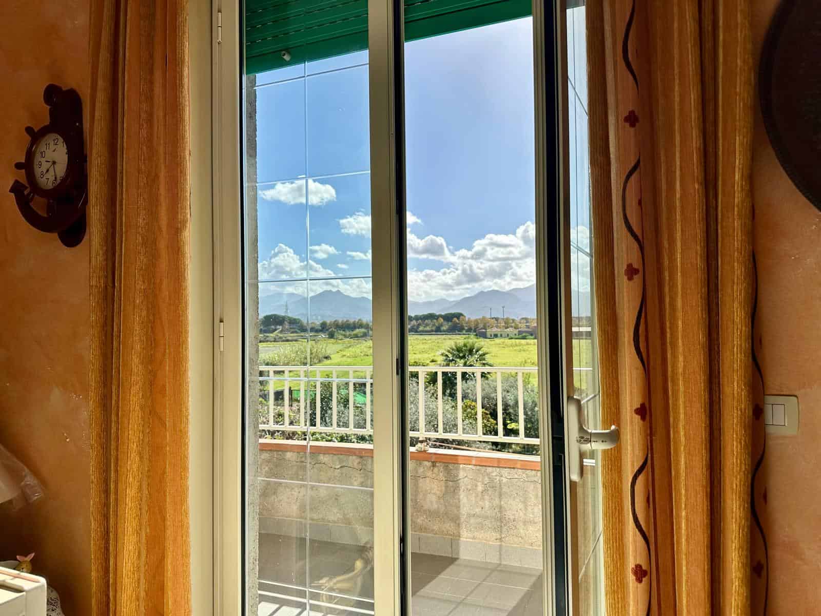 Vista panoramica sulla campagna e sulle montagne dal balcone di una casa con porta finestra, ambiente accogliente arredato in stile tradizionale.
