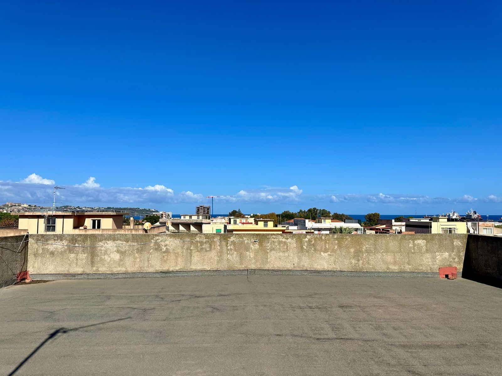 Vista panoramica su tetto di edificio e skyline urbano con mare in lontananza sotto un cielo sereno e azzurro, ideale per immobili residenziali e commerciali di NextCasa.