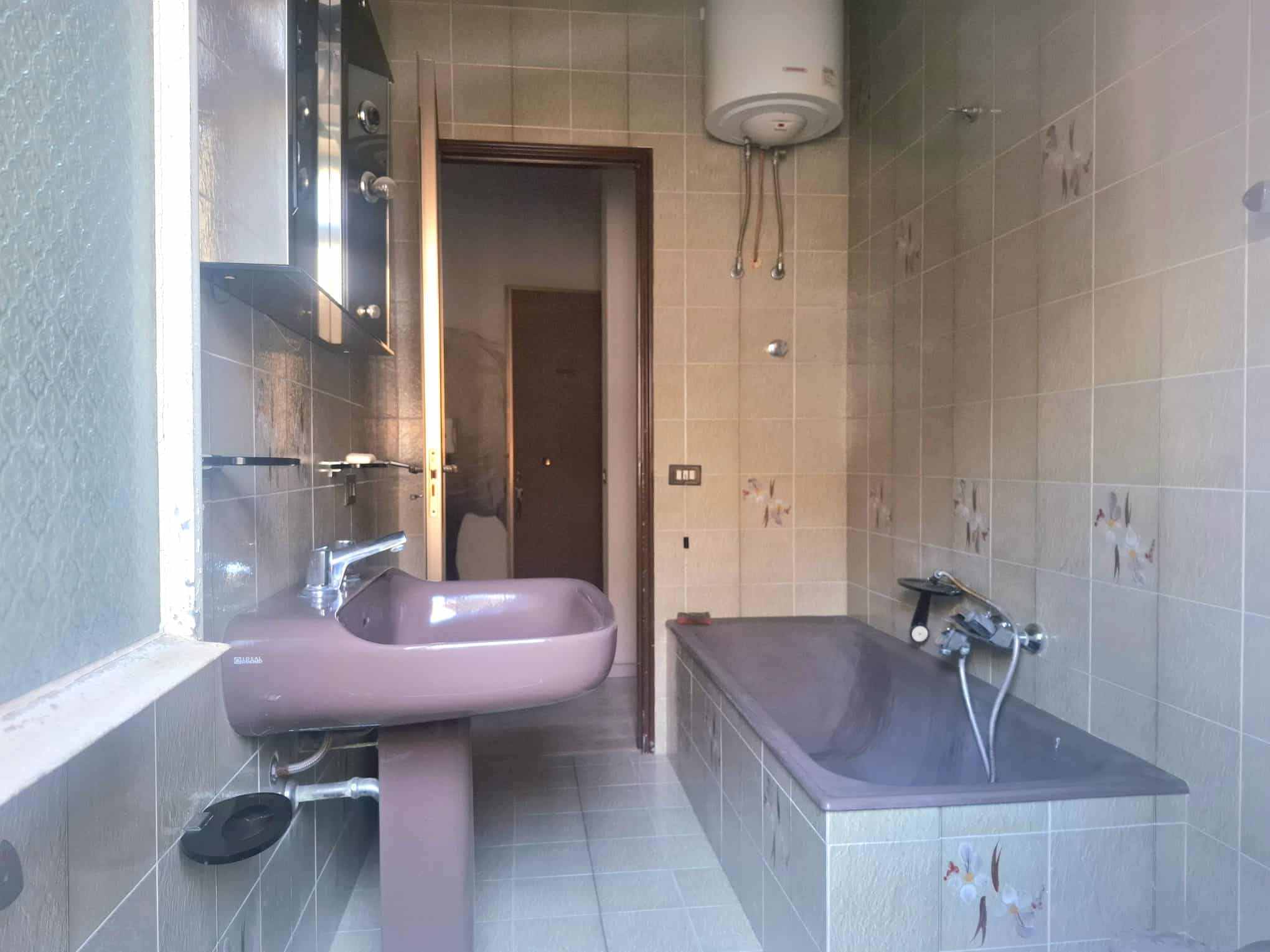 Lavabo e vasca da bagno in un bagno di casa, con pareti rivestite di piastrelle beige e accessori essenziali.