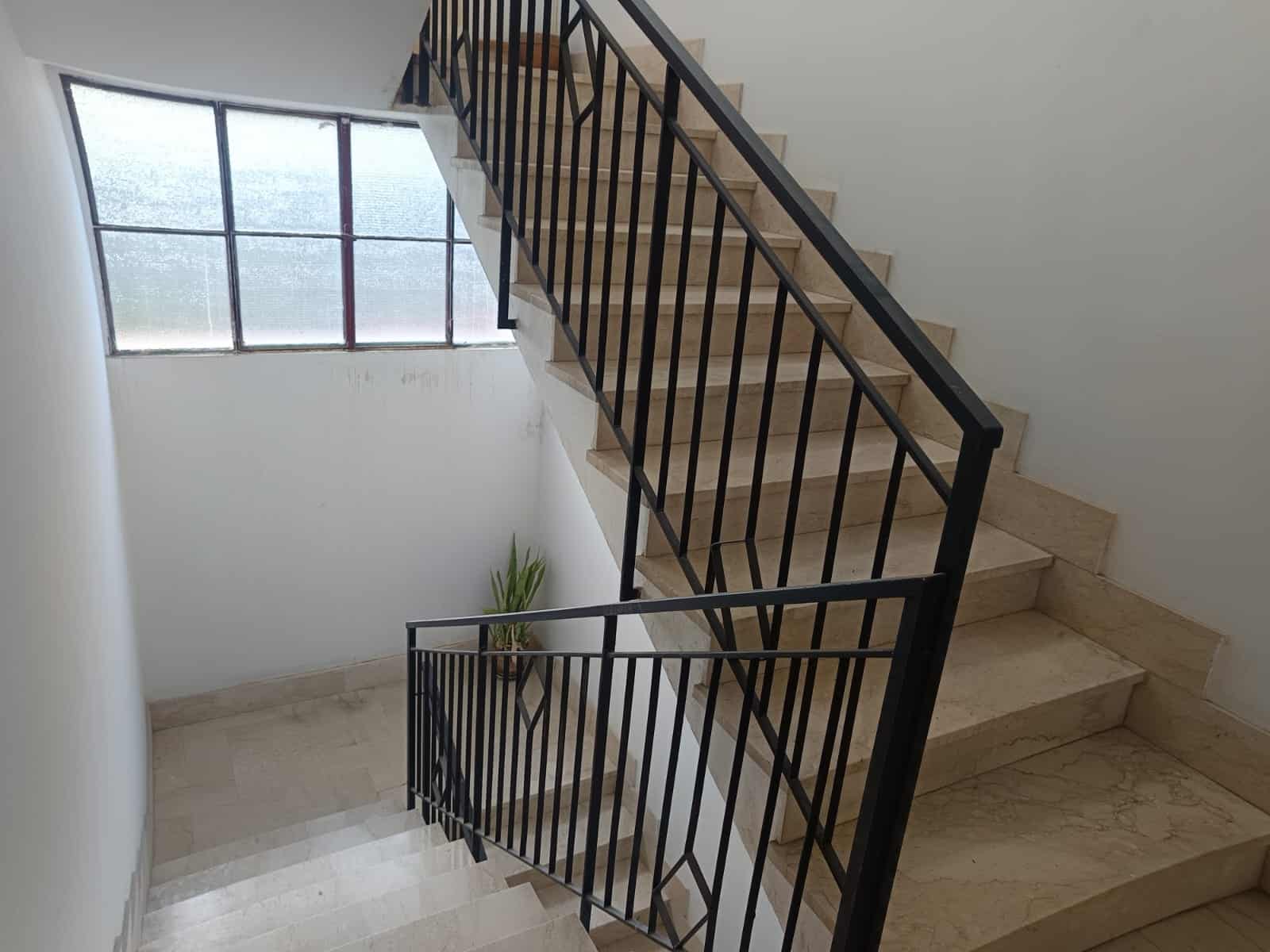 Scale interne in marmo con ringhiera in metallo nero, ambiente luminoso con grande finestra in vetro satinato, ideale per appartamenti moderni e arredamento elegante.