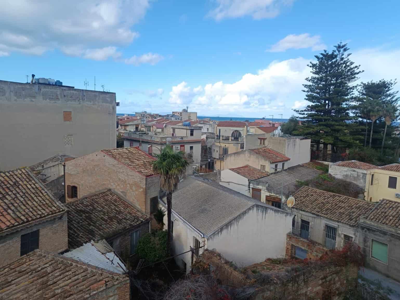 Vista di tetti e case in zona residenziale vicino al mare, con cielo azzurro e nuvole bianche, ambientazione tranquilla e caratteristica qualità edilizia.