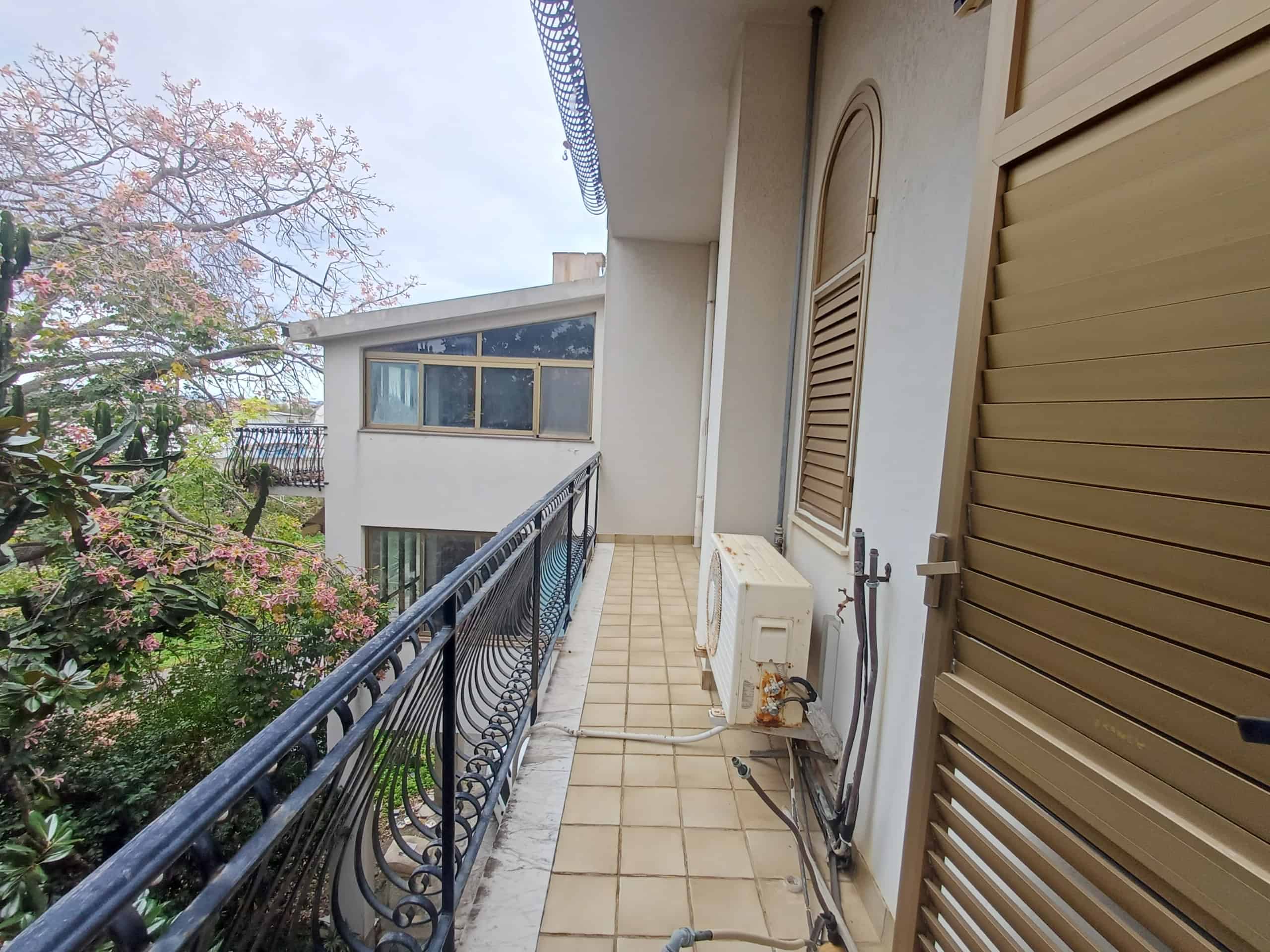 Balcone di un appartamento con ringhiera in ferro battuto e vista su alberi e altre abitazioni, ambiente panoramico e luminoso, ideale per relax e momenti all'aperto.