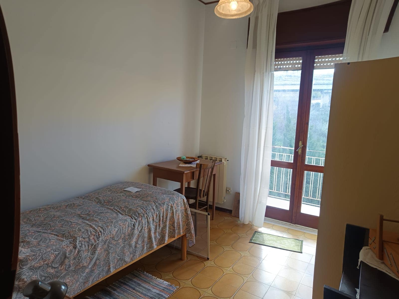 1. Camera da letto con balcone, mobili in legno, tende leggere e ambiente luminoso, ideale per affitti turistici o residenziali in Italia.