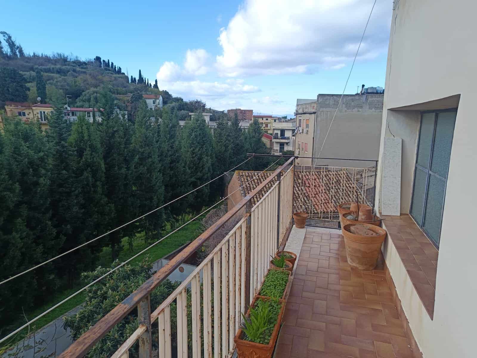 Balcone panoramico con vaso di fiori e vista su alberi e case in quartiere residenziale, ideale per relax e godersi la natura.