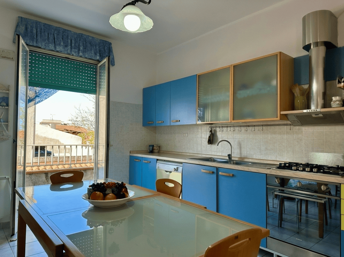 Lavagna da cucina moderna con mobili azzurri, piano cottura e finestra che dà sulla terrazza, ambiente luminoso e accogliente, ideale per soggiorni confortevoli.