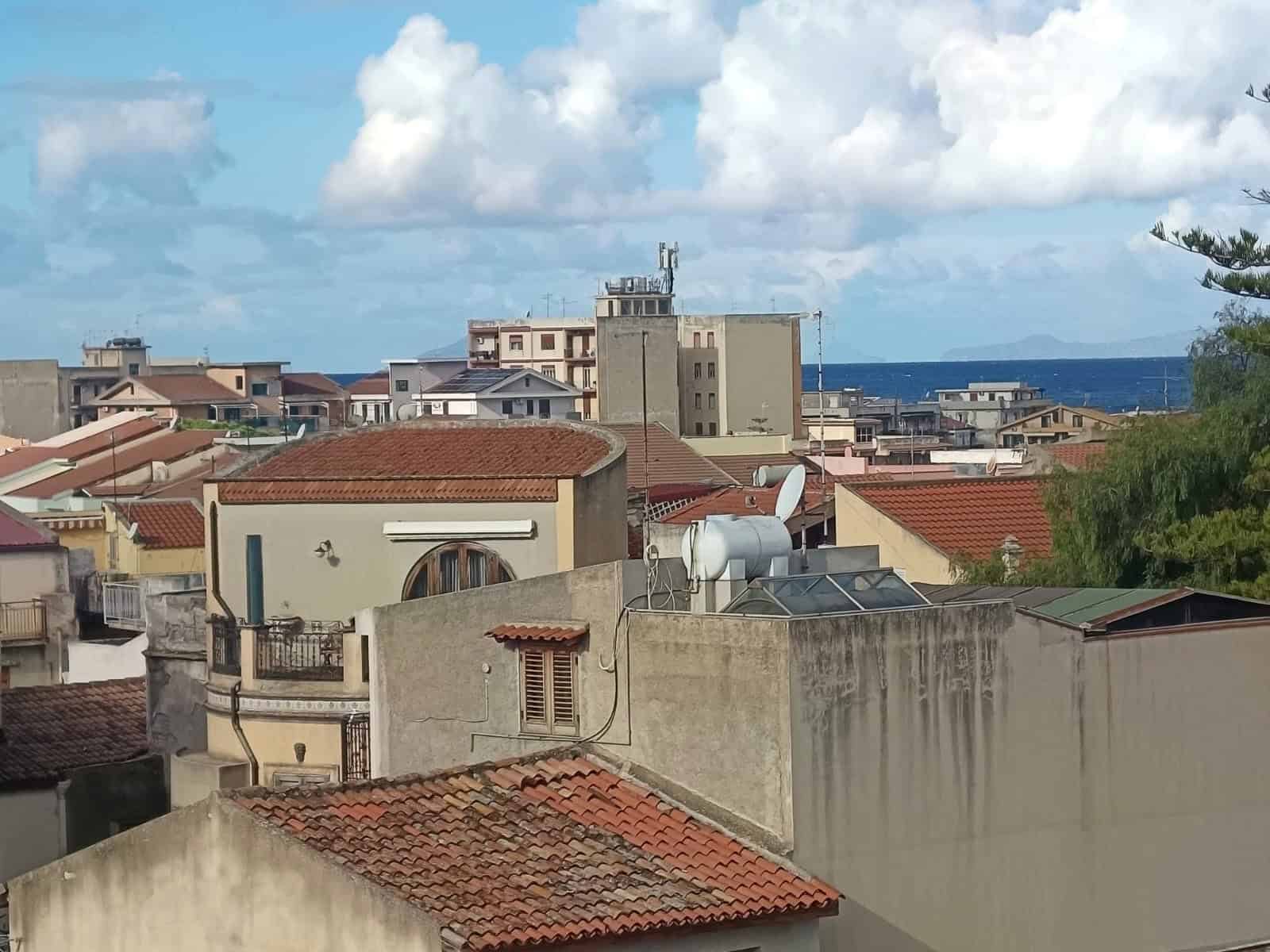 Vista di tetti e edifici residenziali sul mare, con cielo nuvoloso, a poca distanza dalla costa, fotografia di panorama urbano in stile mediterraneo, con caratteristiche case italiane.