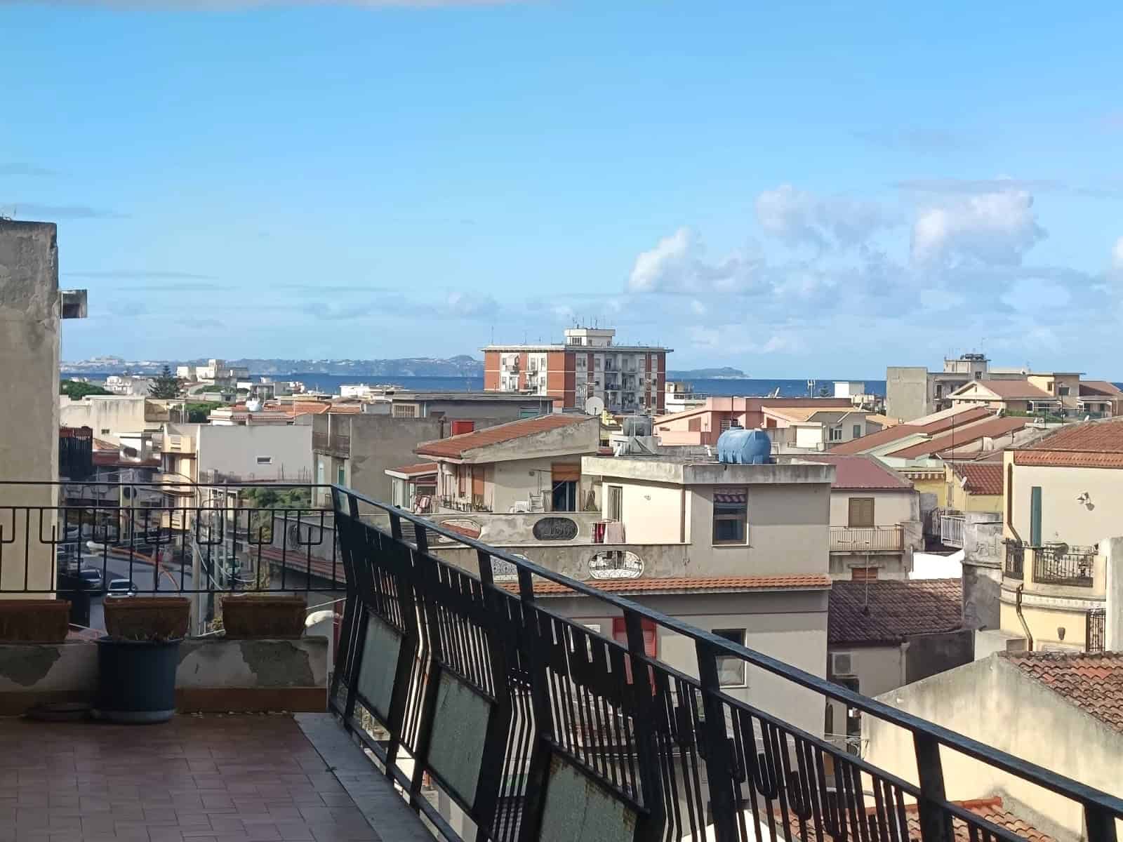 Vista panoramica di un quartiere residenziale con tetti di tegole, edilizia moderna e mare sullo sfondo, resa ideale per annunci immobiliari e proprietà in vendita o affitto in area urbana costiera.