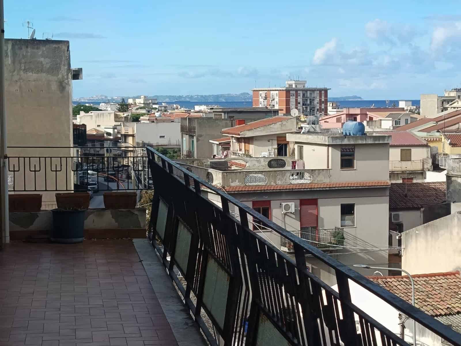 Balcone con vista mare e tetti di città, edificio residenziale con skyline blu, architettura urbana, spazio esterno panoramico, atmosfera di città costiera italiana.