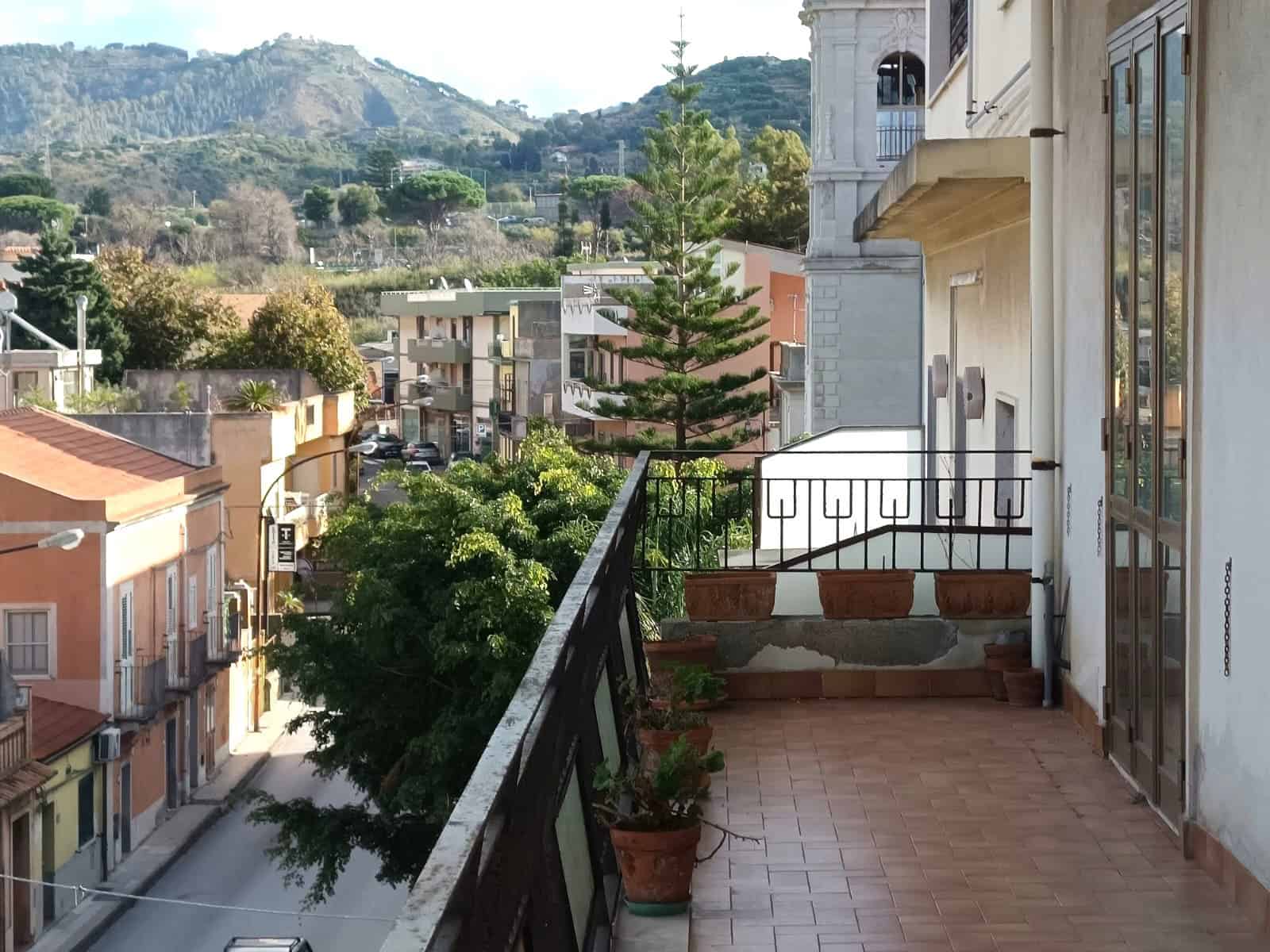 Balcone con vista sulla città e sulle montagne, con piante in vaso, illustrazione di un'abitazione con stile classico e modernità, ideale per chi cerca immobili in vendita o affitto a Napoli, Italia.