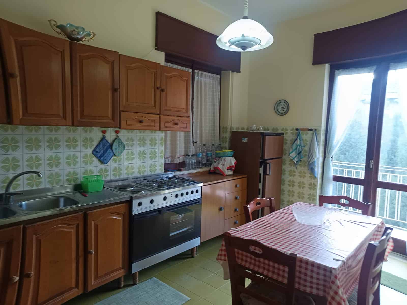 1. Cucina classica con mobili in legno, piano cottura e frigorifero, ideale per ambienti abitativi accoglienti e funzionali.