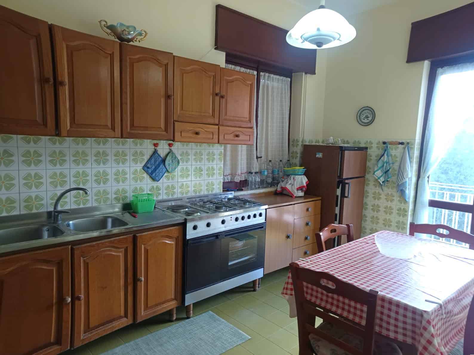 1. Cucina abitabile con ante in legno, piano cottura a gas, frigorifero e tavolo con tovaglia a scacchi rossi e bianchi, ambiente luminoso e accogliente.