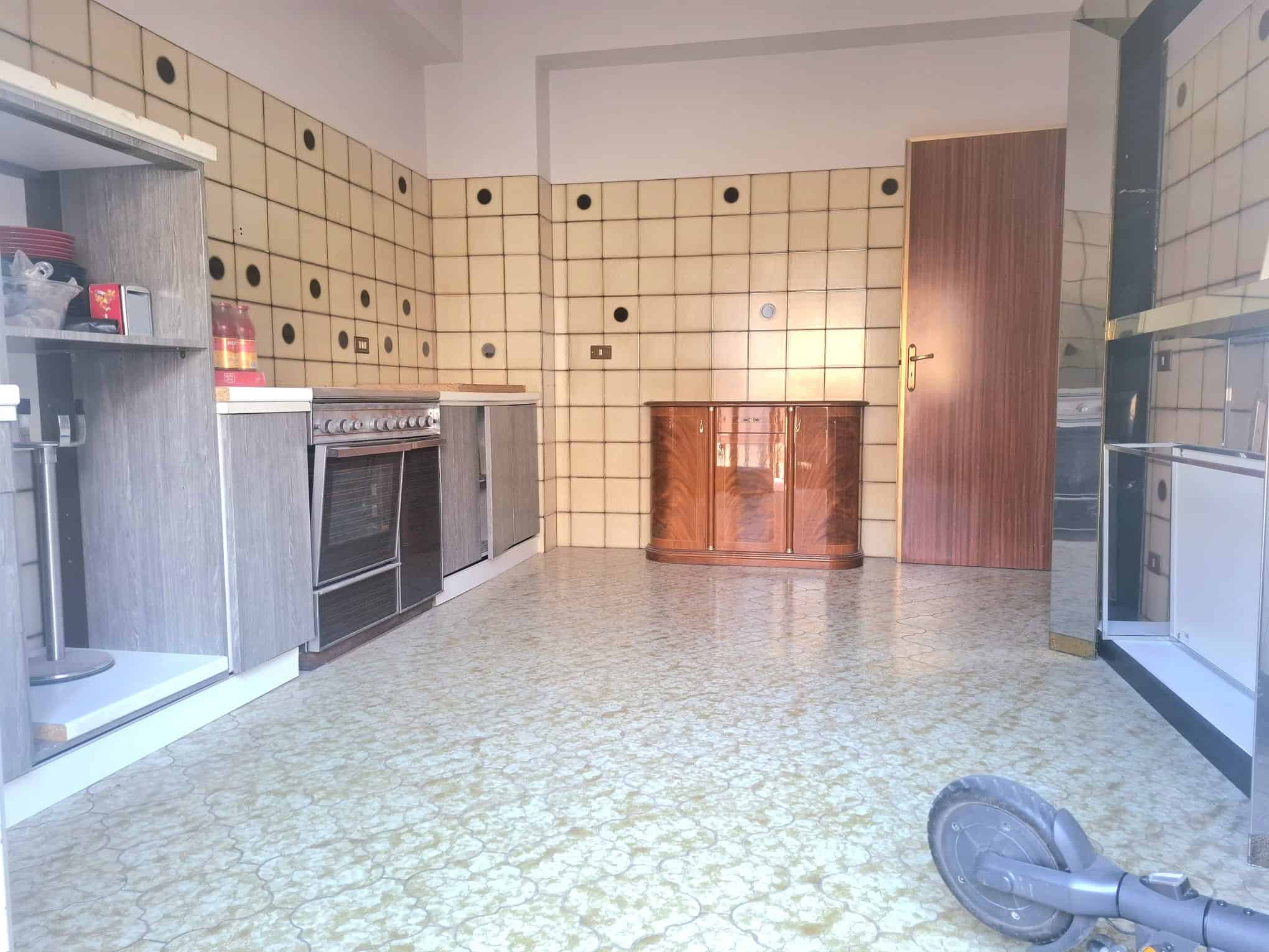 Cucina spaziosa con pareti rivestite di piastrelle beige e nero, elettrodomestici moderni e pavimento in marmo chiaro, ideale per famiglie e cucine funzionali.