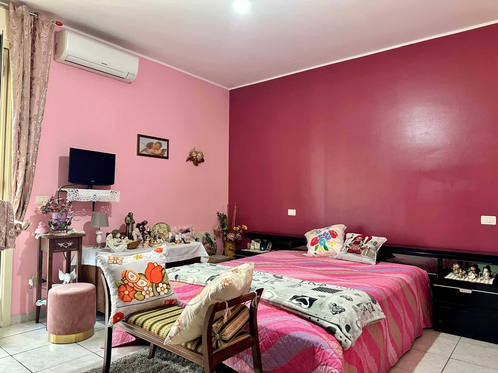 Letto matrimoniale camera da letto con pareti rosa e decorazioni floreali, ambiente accogliente e ben arredato, ideale per famiglie che cercano una soluzione di comfort e stile.