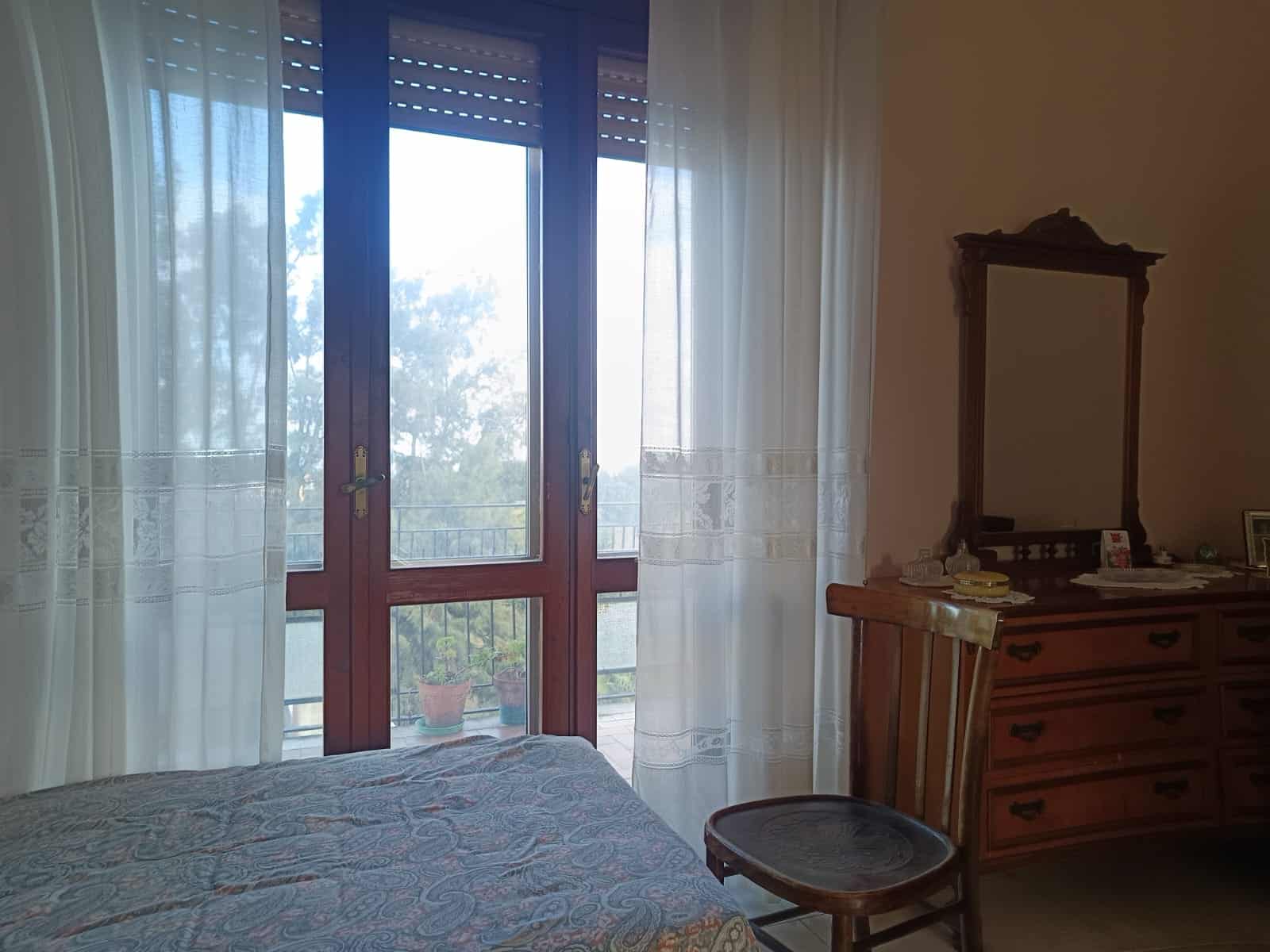 Vista camera matrimoniale con balcone, tende leggere e arredamento classico, ambiente luminoso e confortevole, ideale per vivere in tranquillità.