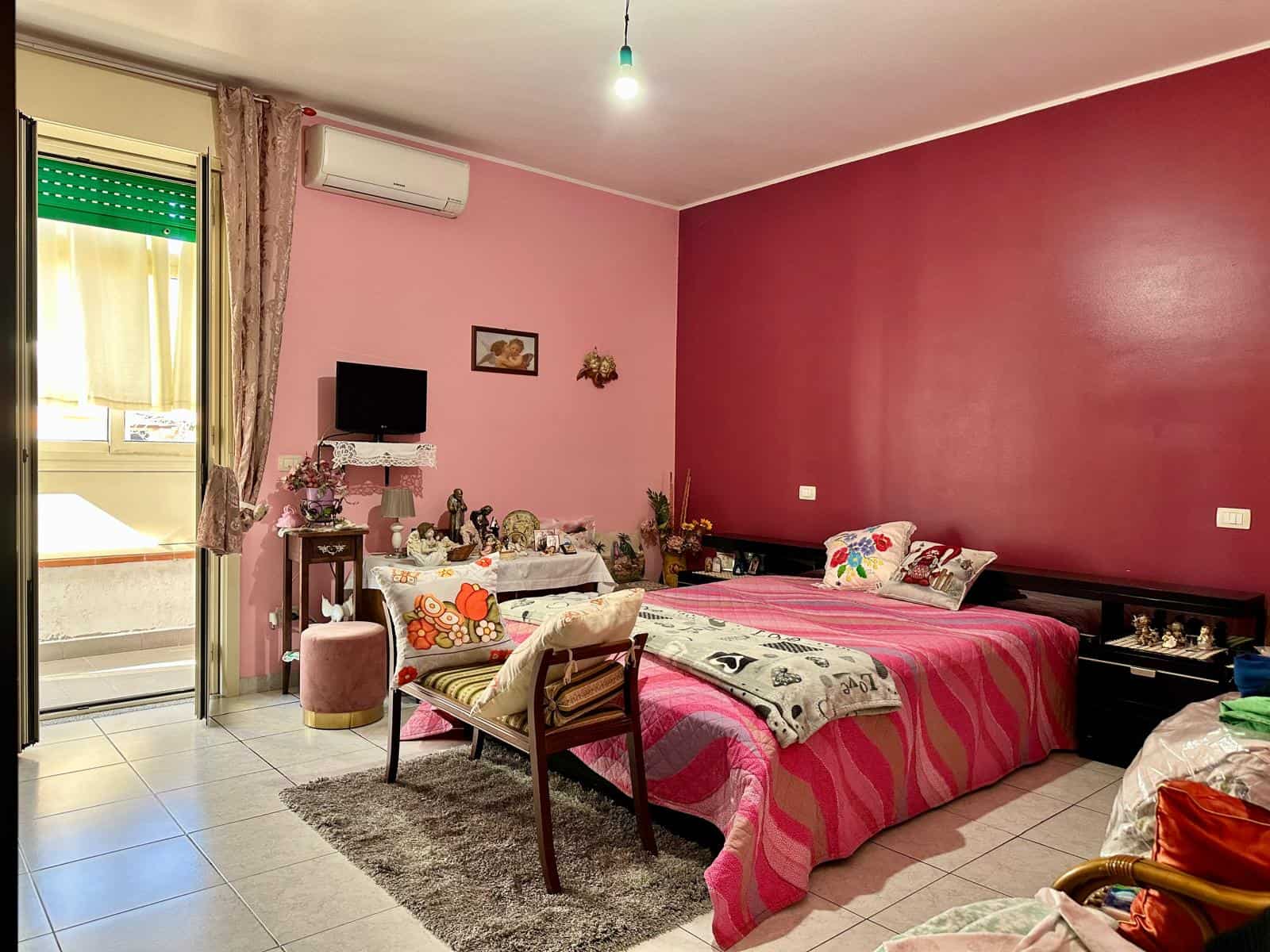 Letto matrimoniale con testiera moderna in cameretta decorata con tende e oggetti d'antiquariato, spazio accogliente con pareti rosa, arredi funzionali e decorazioni vintage, ideale per ambienti di soggiorno o camera da letto.