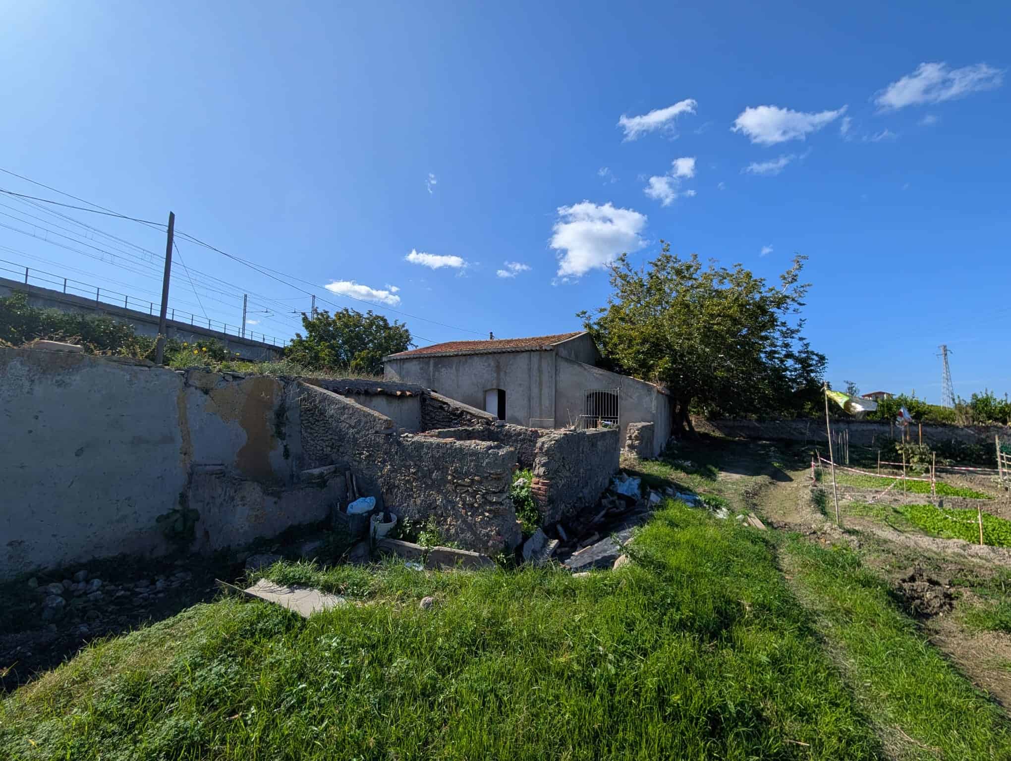 Vecchio rifugio di campagna in mattoni e cemento, immerso in un contesto rurale con vegetazione verde e cielo sereno, perfetto per investimenti immobiliari rurali.