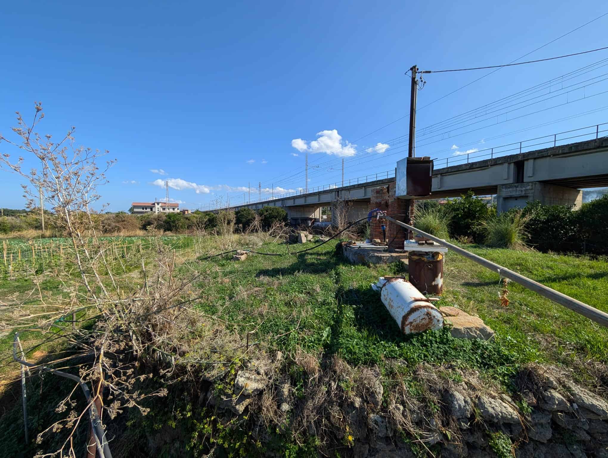 Titolare di Italia, nuvole e cielo blu sopra un treno sopraelevato con area verde e rocciosa sottostante, presenza di infrastruttura ferroviaria e natura circostante, ambientazione open air.