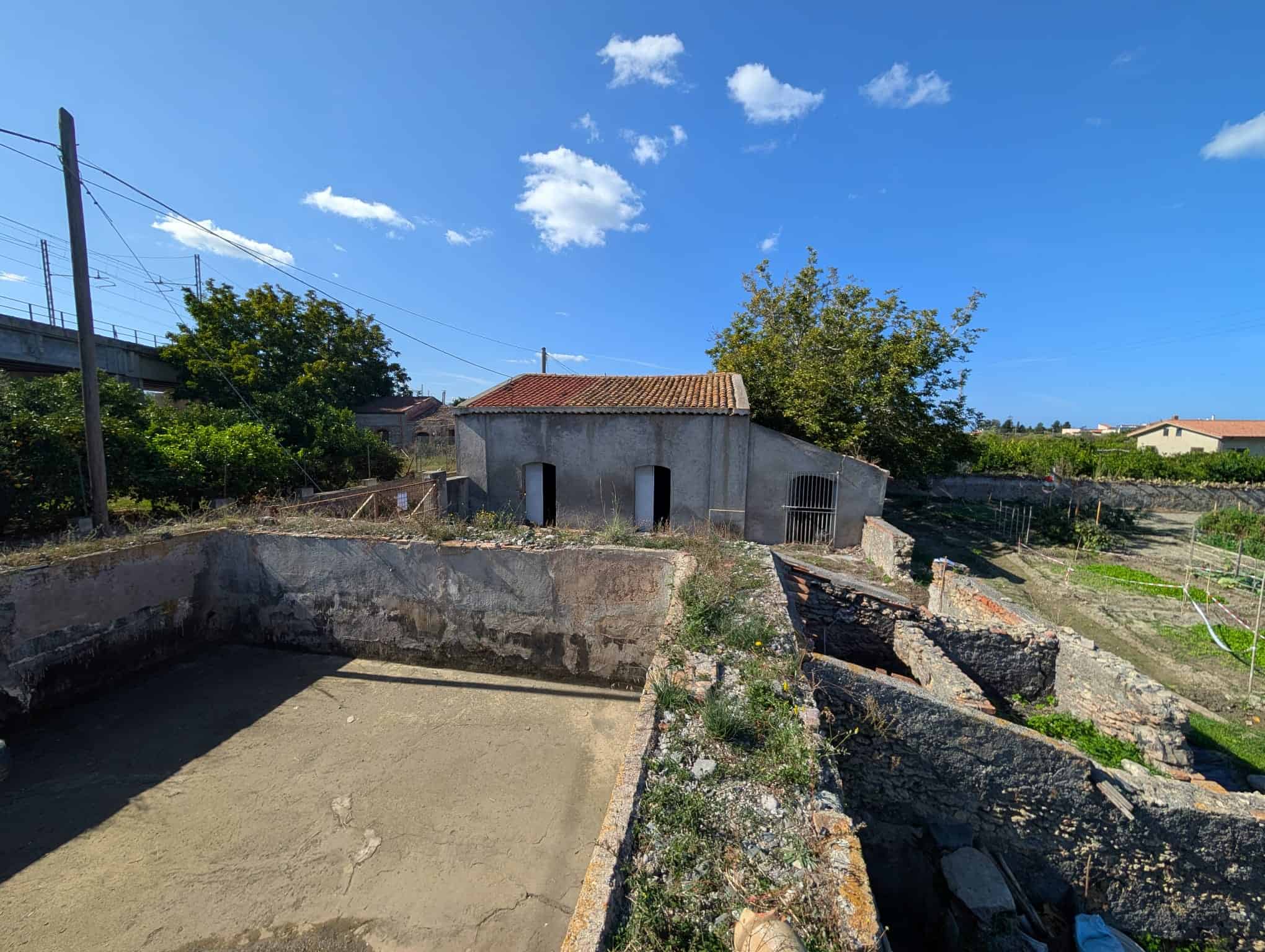 Cantiere di ristrutturazione edilizia con vecchie strutture e terreno pronto per nuovi progetti immobiliari.