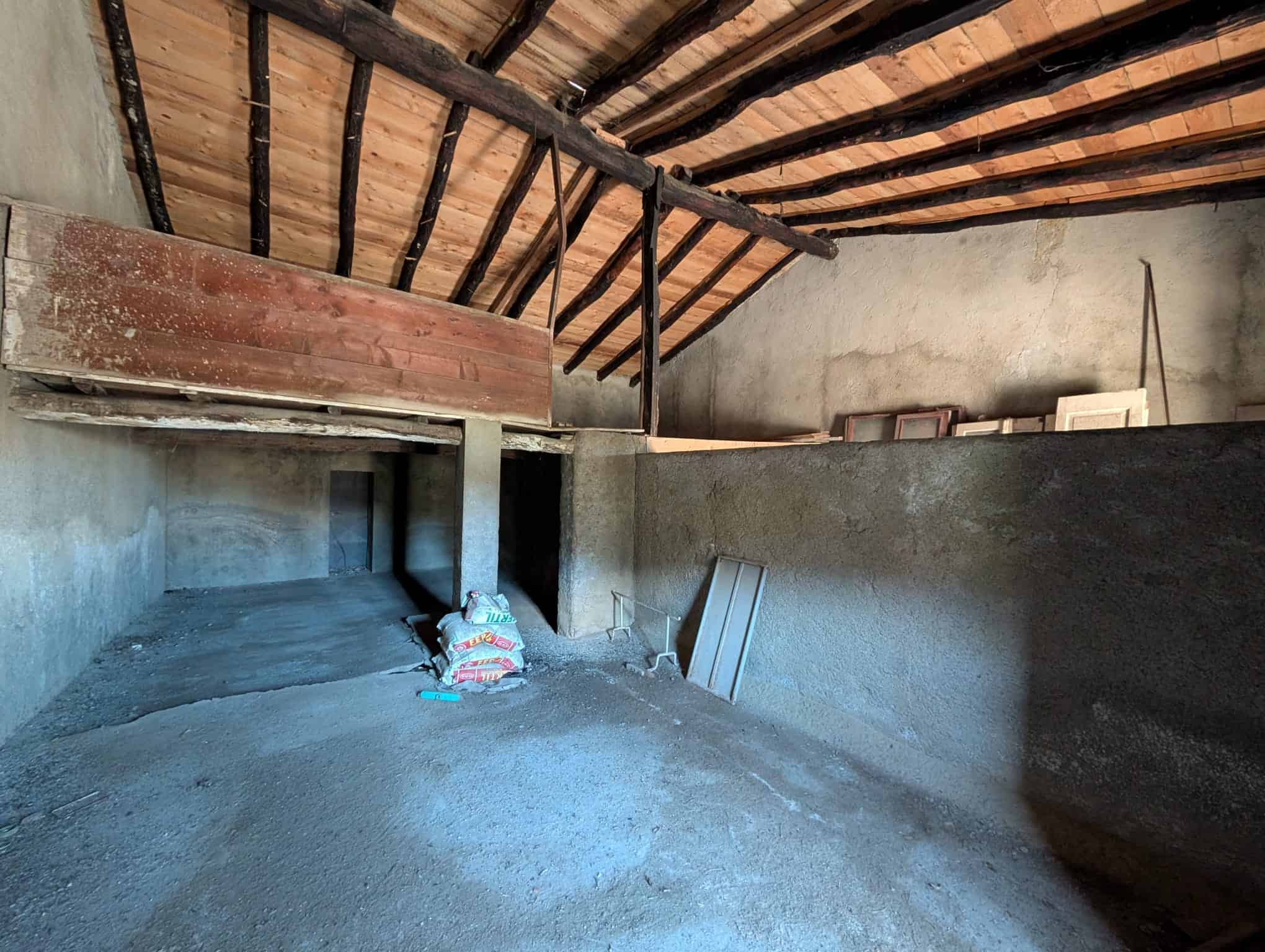 Vecchia soffitta in costruzione con travi in legno e pareti in cemento, spazio in fase di ristrutturazione per realizzare una soffitta di design.