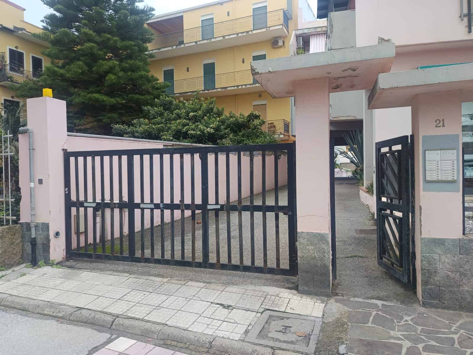 Cancello di ingresso e cortile di un appartamento in residence a Napoli, ingresso con recinzione in ferro nero, strada e edifici residenziali sullo sfondo.