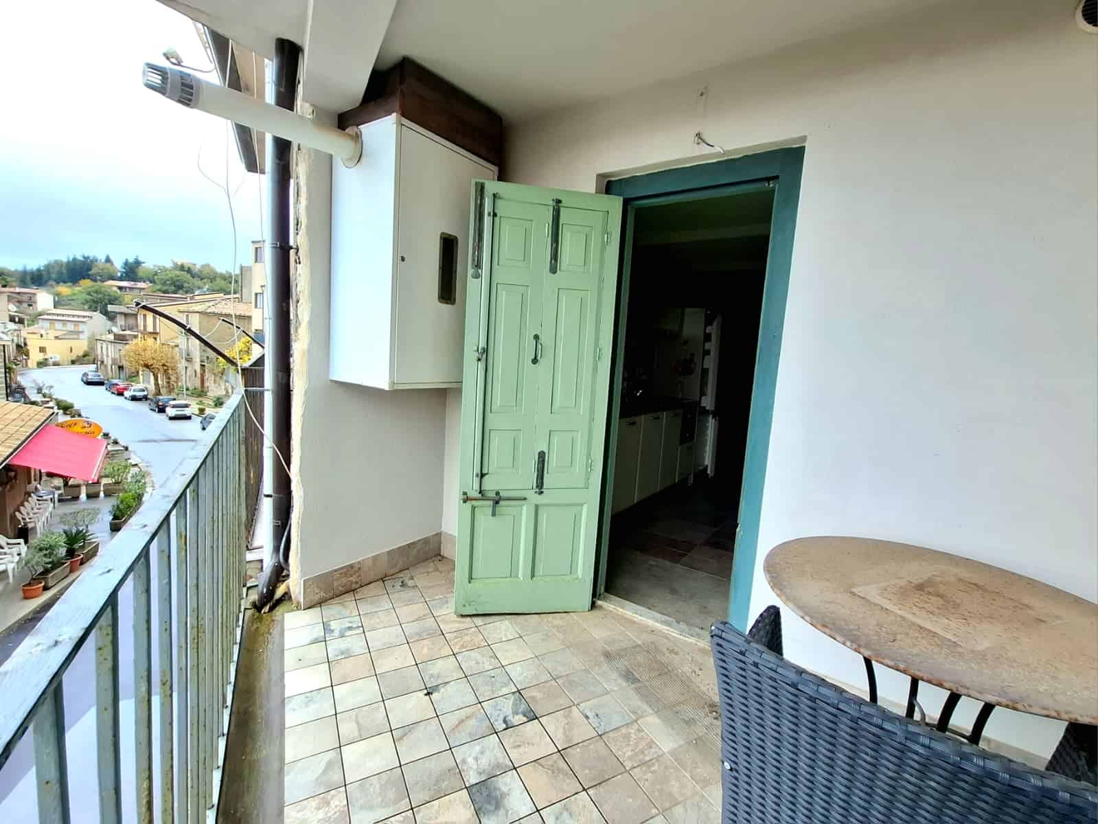 Balcone con accesso alla cucina, vista sulla strada e sul quartiere, pavimentato in piastrelle, con tavolo e sedia in rattan, ideale per relax e colazioni all'aperto.