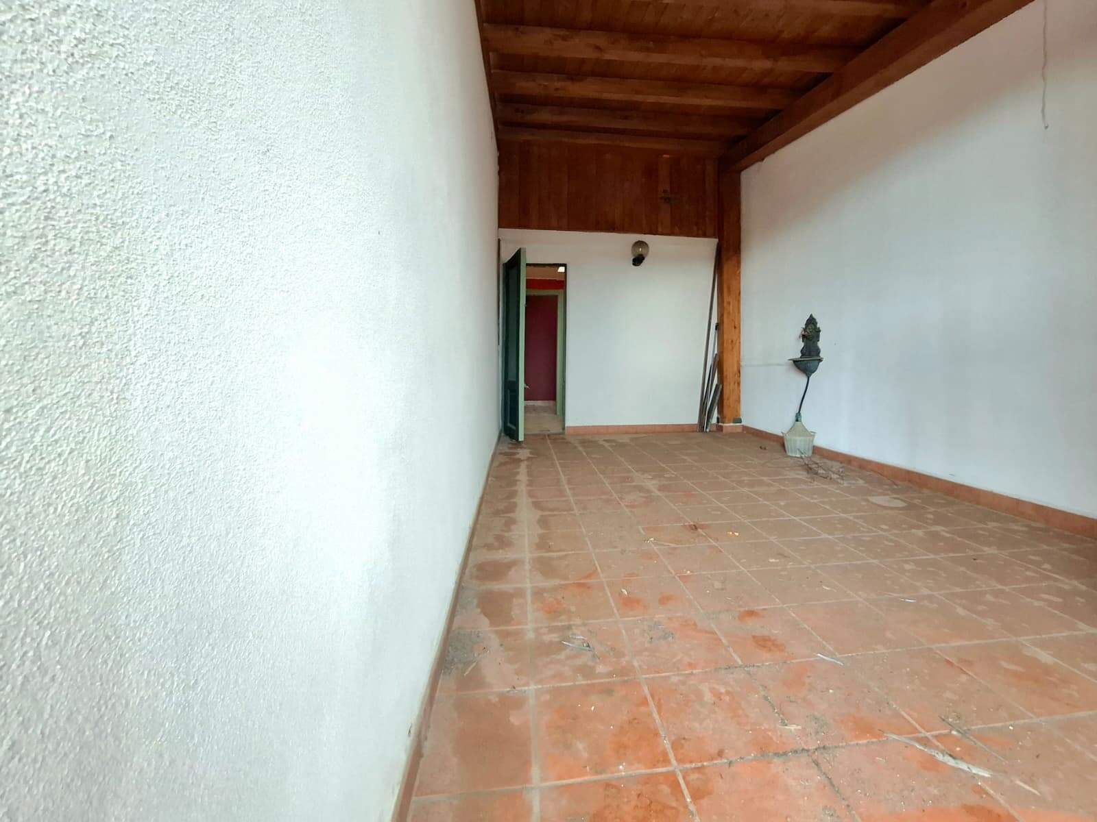Spazio esterno in terracotta con pareti bianche e soffitto in legno, ideale come terrazza o area relax all'aperto.