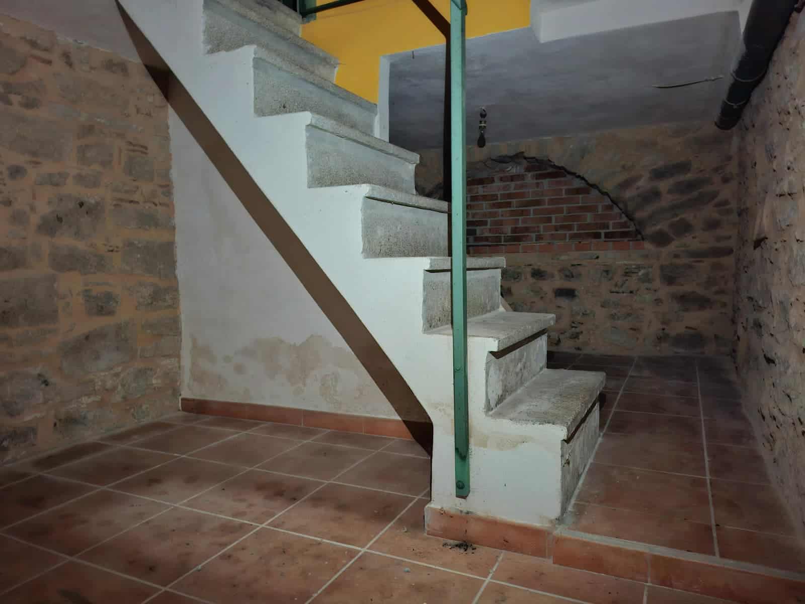 Scala interna in pietra con muro di mattoni a vista e pavimento in ceramica, ambiente rustico in fase di ristrutturazione a NextCasa.