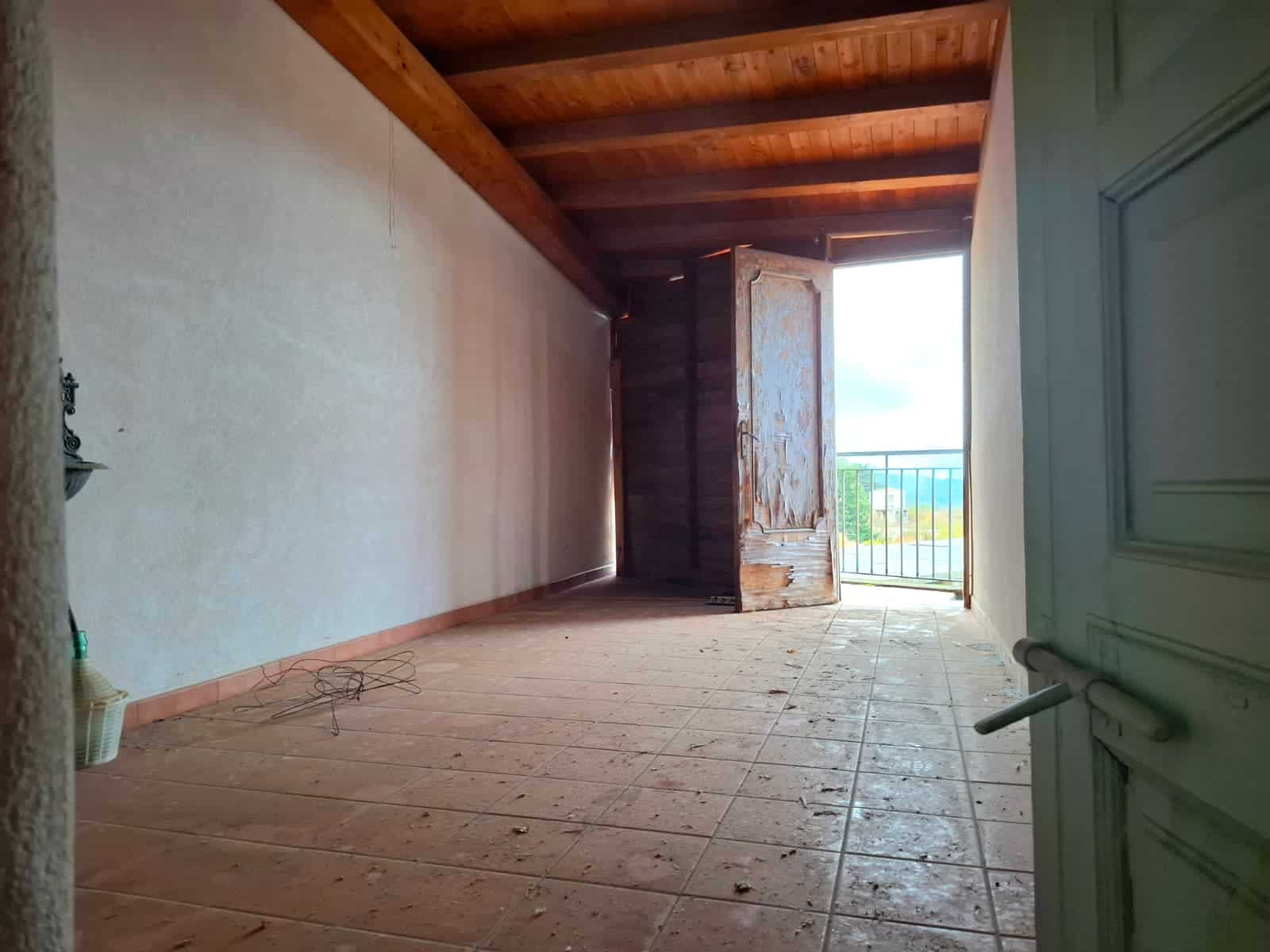 Spazio vuoto in un appartamento con soffitto in legno e porta finestra che dà su un balcone con vista panoramica. Perfetto per ristrutturazione e personalizzazione.