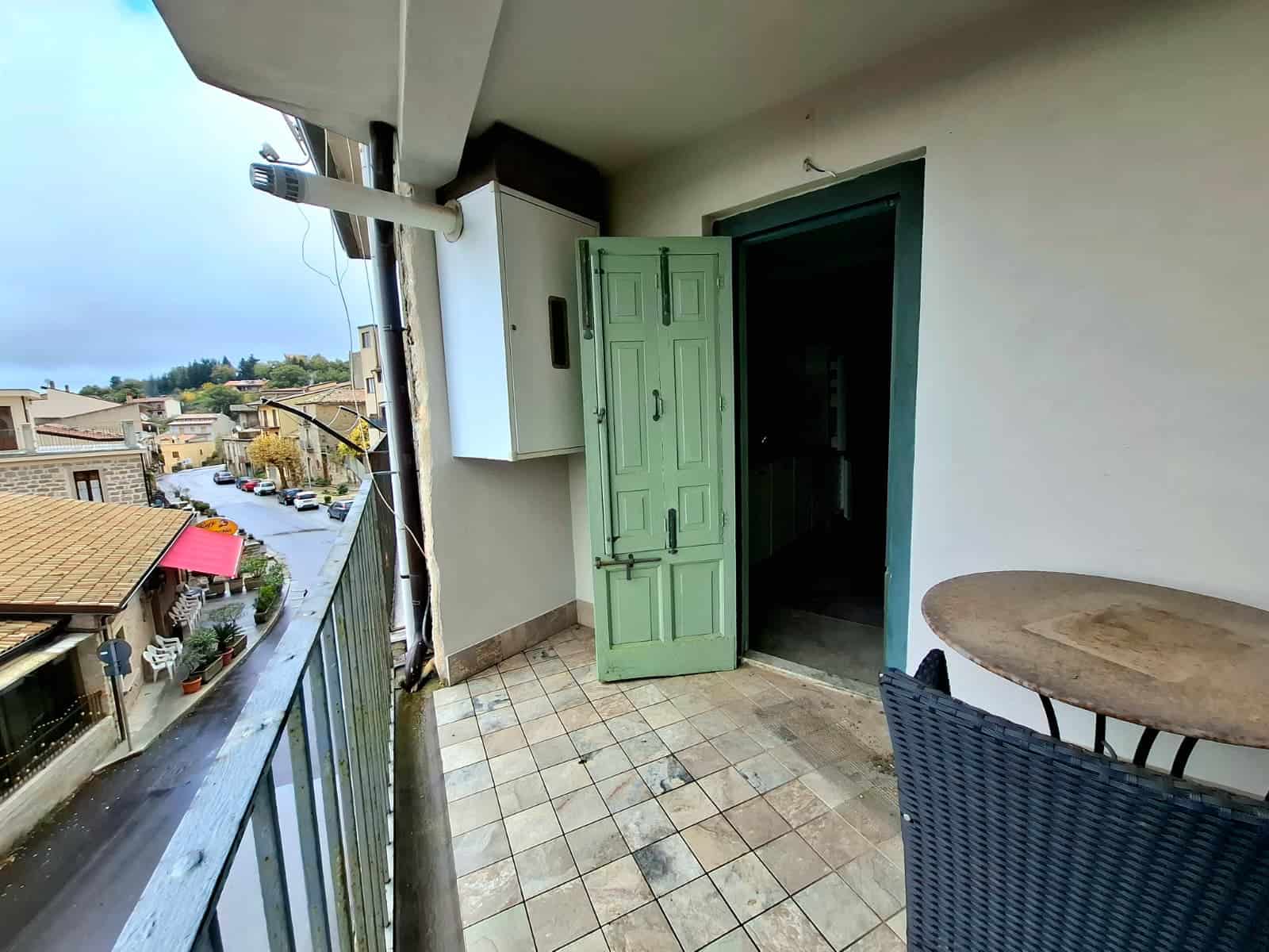 Balcone di un appartamento in affitto a NextCasa, con vista sul paese, arredato con tavolo e sedia, ideale per relax e vivere all'aperto.