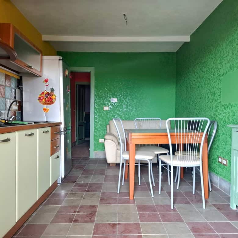 Colorato e accogliente ambiente cucina con mobili verdi, pavimento in piastrelle e pareti vivaci, tavolo con sedie in metallo e un divano beige, perfetto per vivere momenti di convivialità e relax.