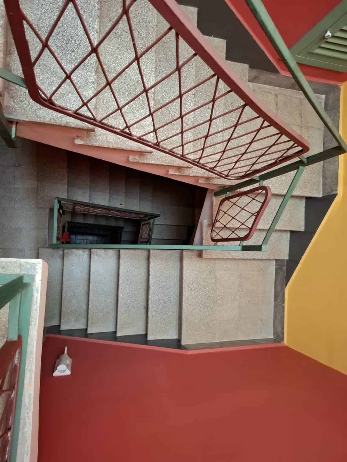 Scale condominiali con ringhiera in ferro battuto, vista dall'alto, all'ingresso di un edificio con pareti colorate e pavimento in pietra, ideale per camere e appartamenti moderni.