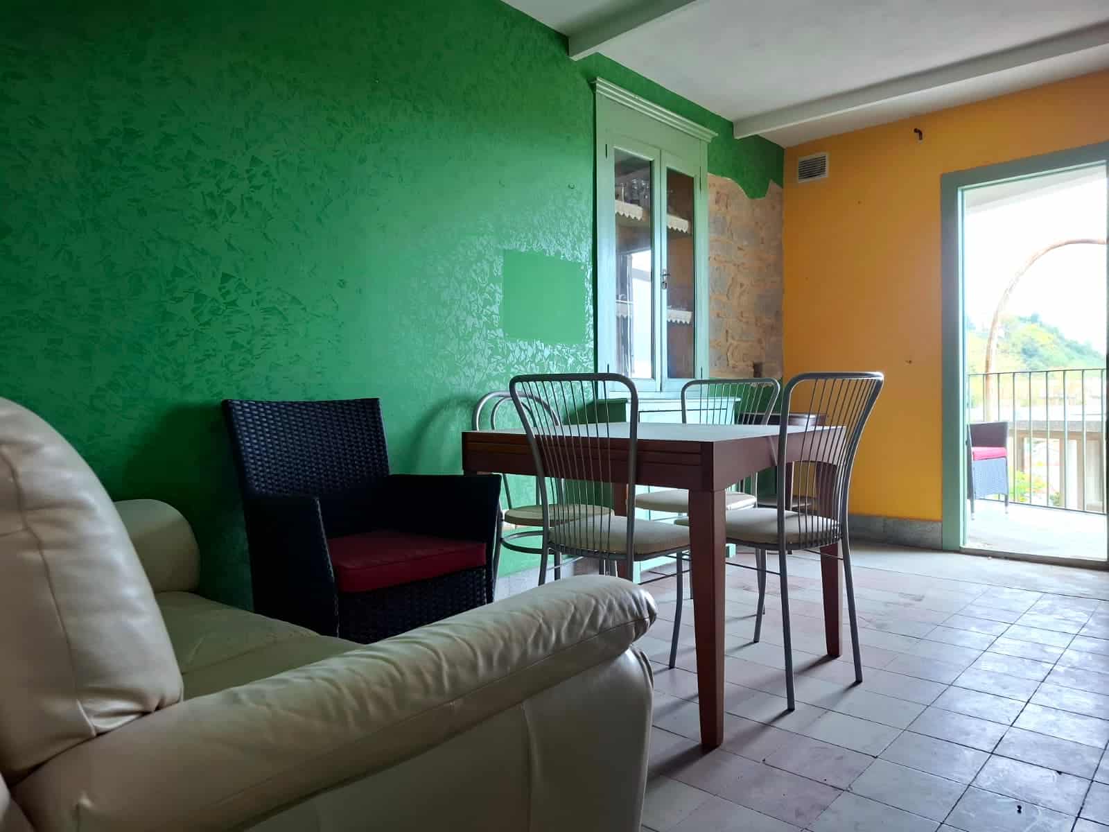 Soggiorno con pareti colorate verde e giallo, mobili per la casa, porta finestra con accesso al balcone, stile rustico, atmosfera accogliente e luminosa, perfetto per appartamenti moderni e colorati.