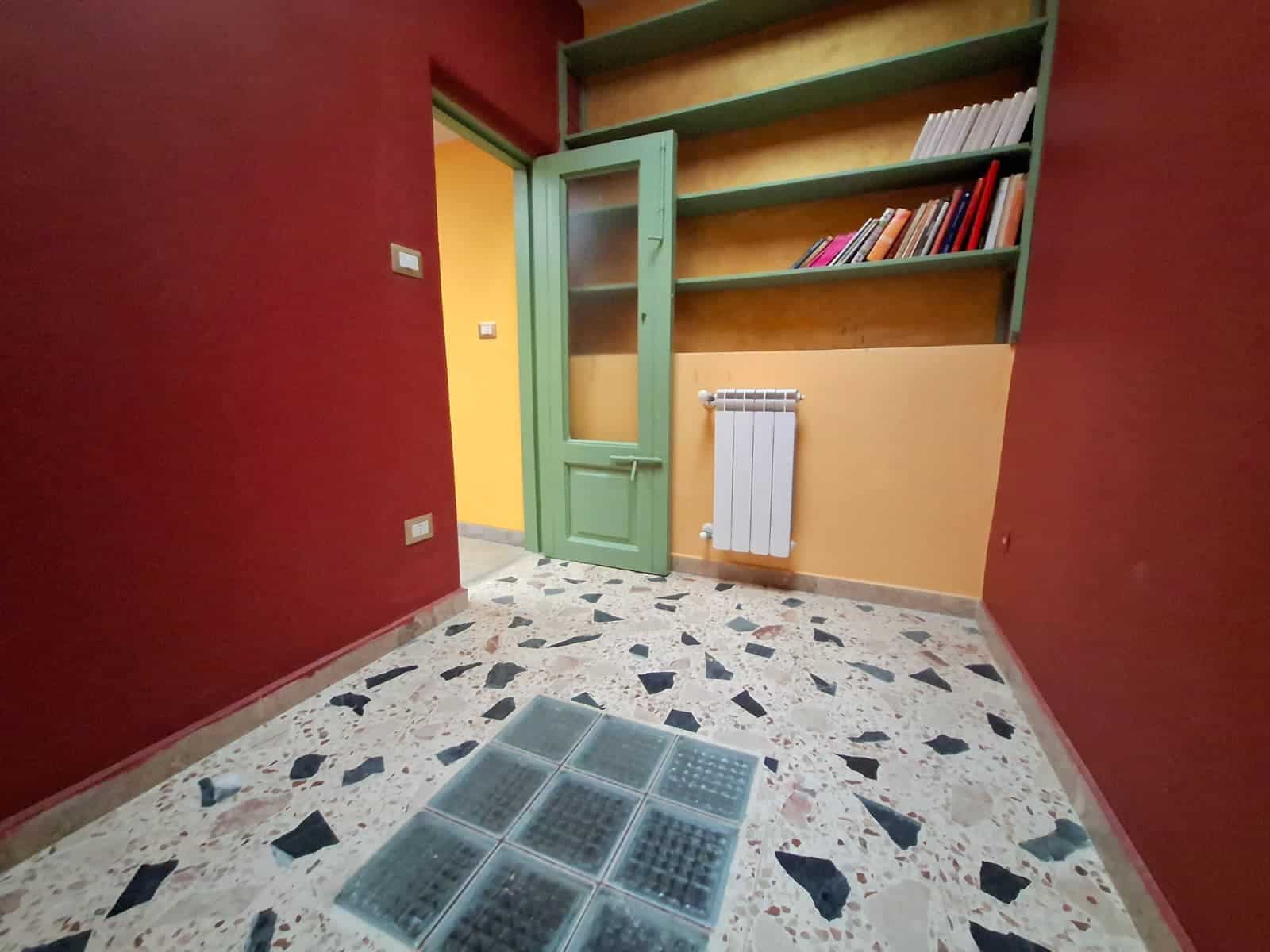 Armadio a muro verde, libreria e porta in legno in un ingresso o corridoio di appartamento, pavimento in piastrelle di marmo, pareti colorate in rosso e giallo, dettagli di arredamento per interni.